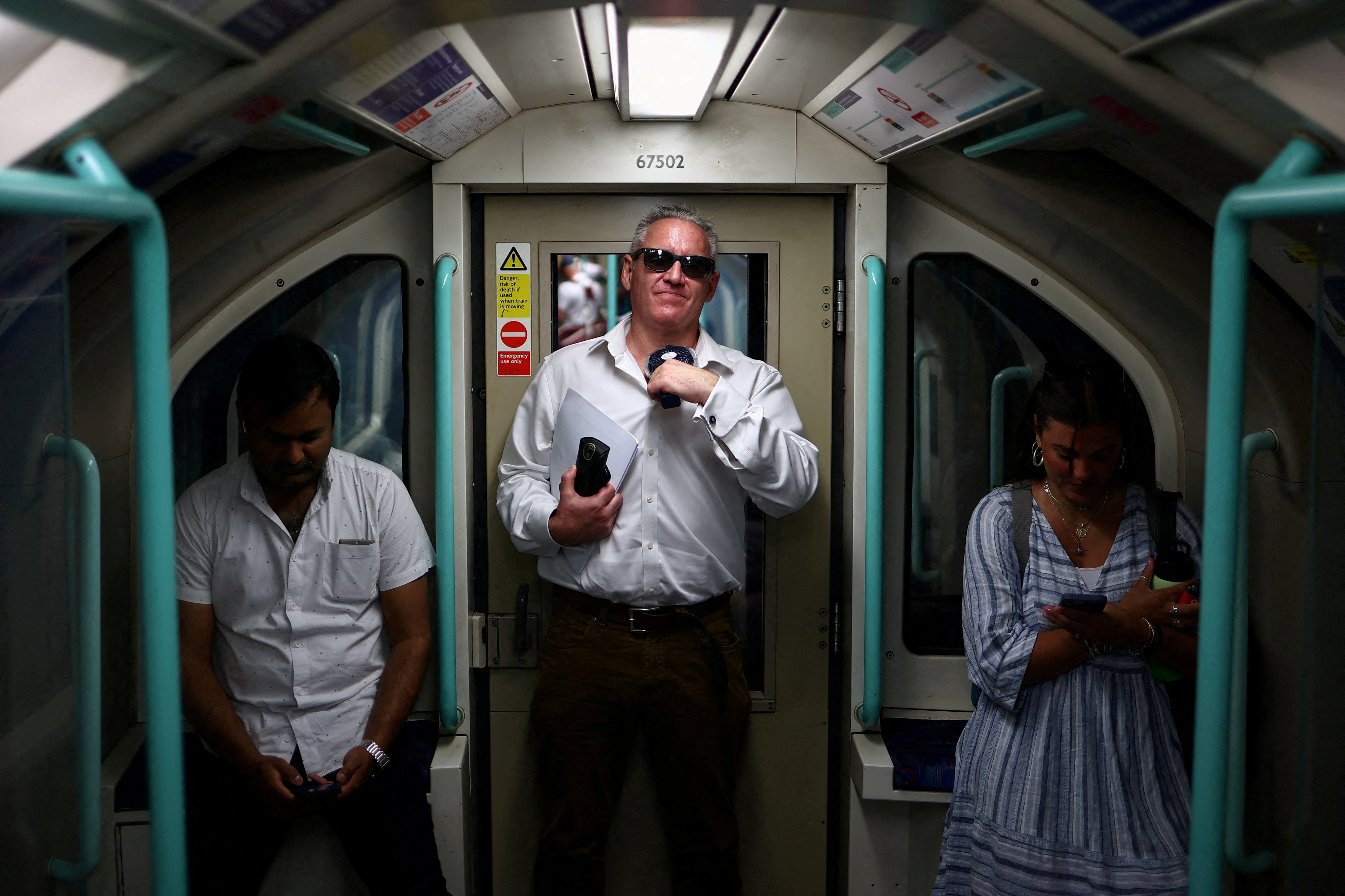 A man uses a fan to cool down while travelling on a train.