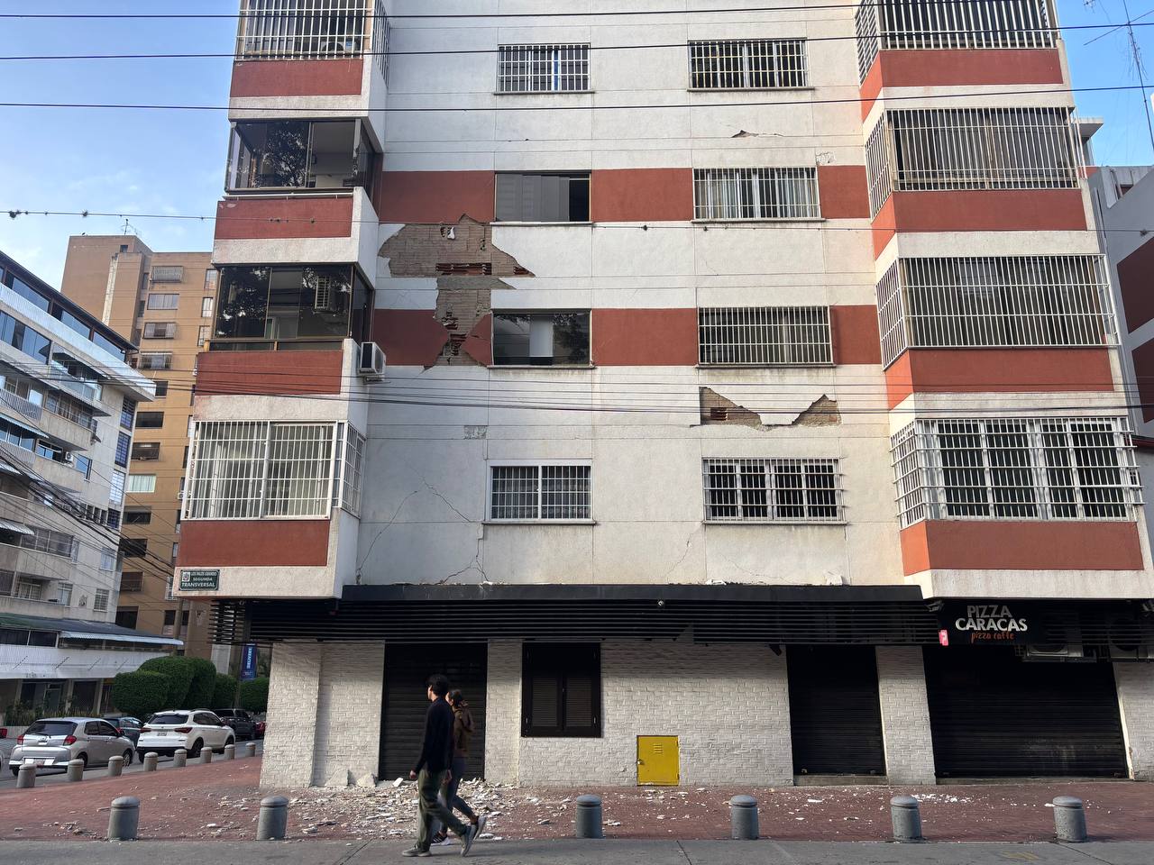 A pair of pedestrians walk by a building in Caracas that suffered damage to its facade during the June 24 earthquakes