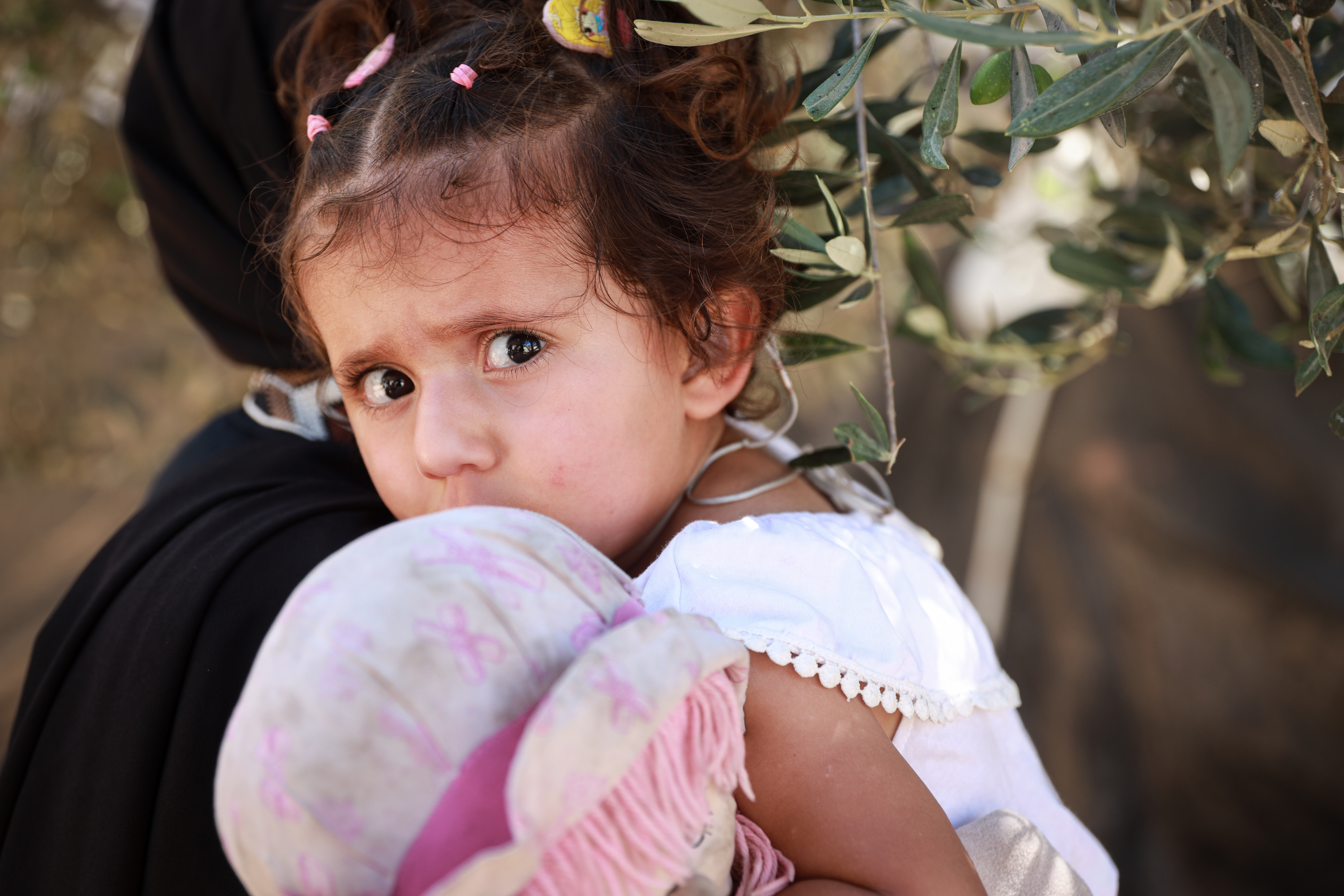 A young child looks on from her mother's shoulder.