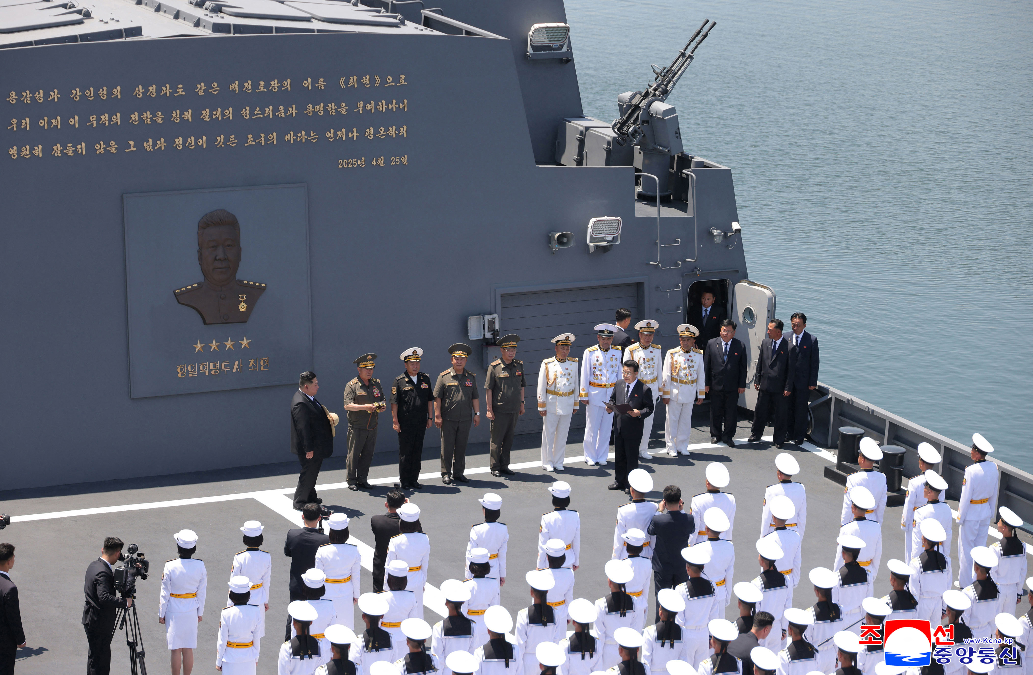 Kim Jong Un stands on the deck of a large grey warship, with naval equipment visible around him.