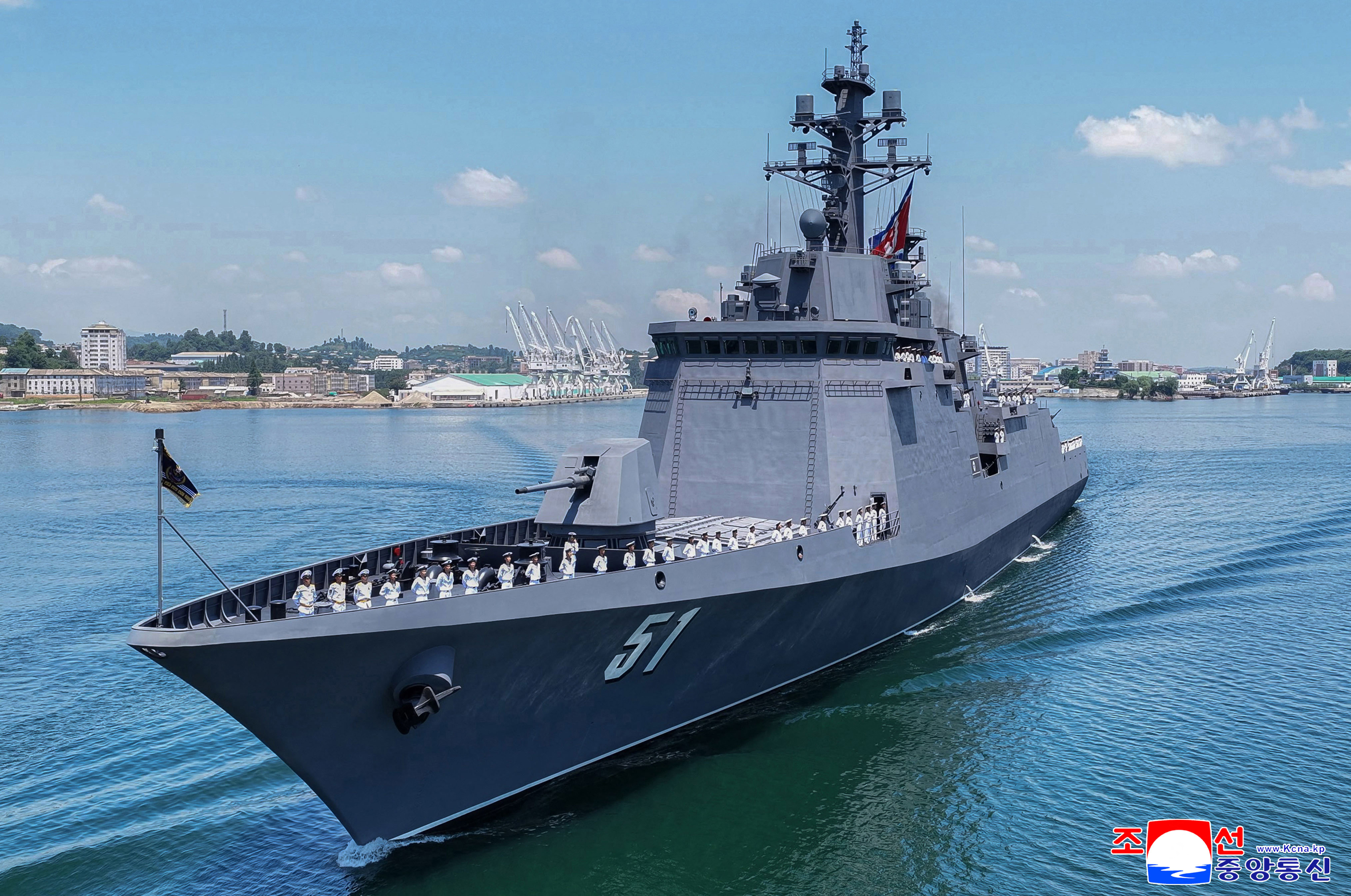 A large grey warship moves through open water, leaving a wake behind it.