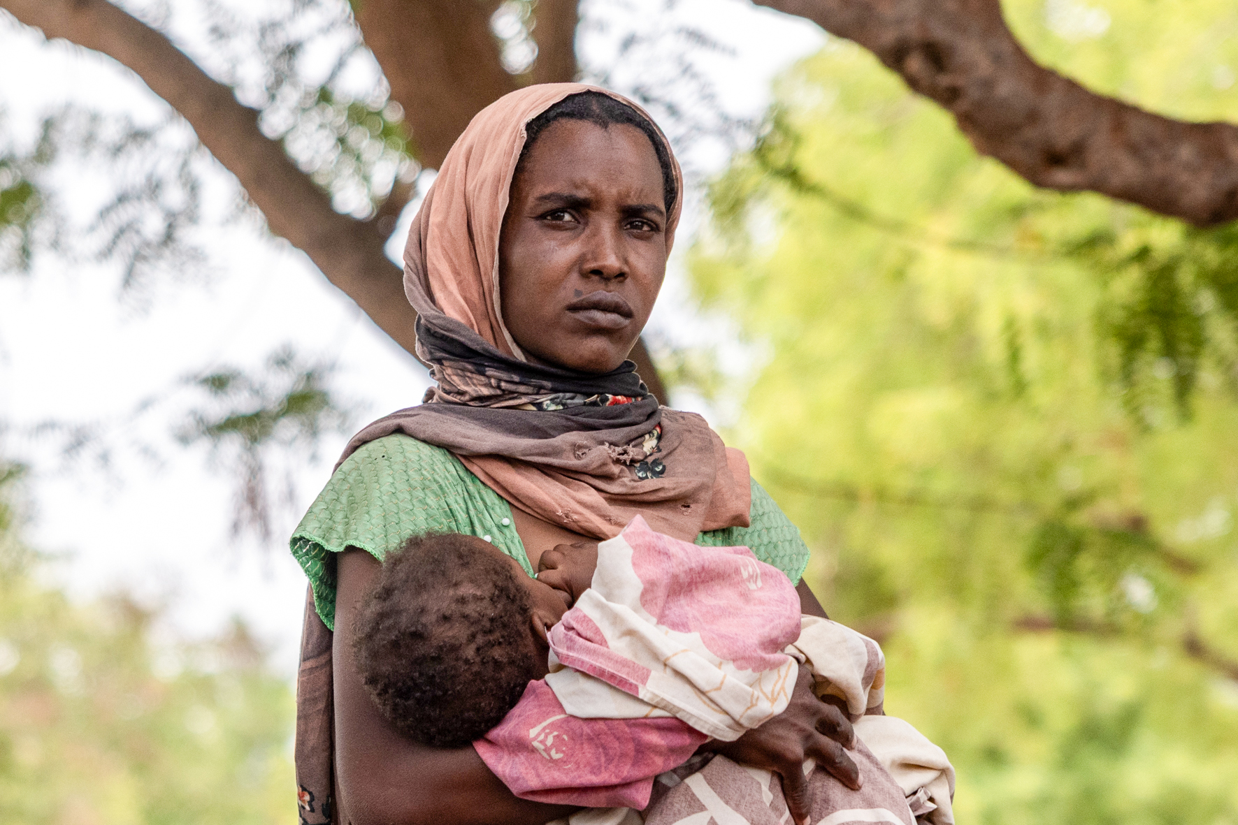 A woman holds her baby outside the registration center for new refugees on the outskirts of the Korsi Refugee Camp in Birao, Central African Republic, Thursday, March 26, 2026. (AP Photo/Caitlin Kelly)