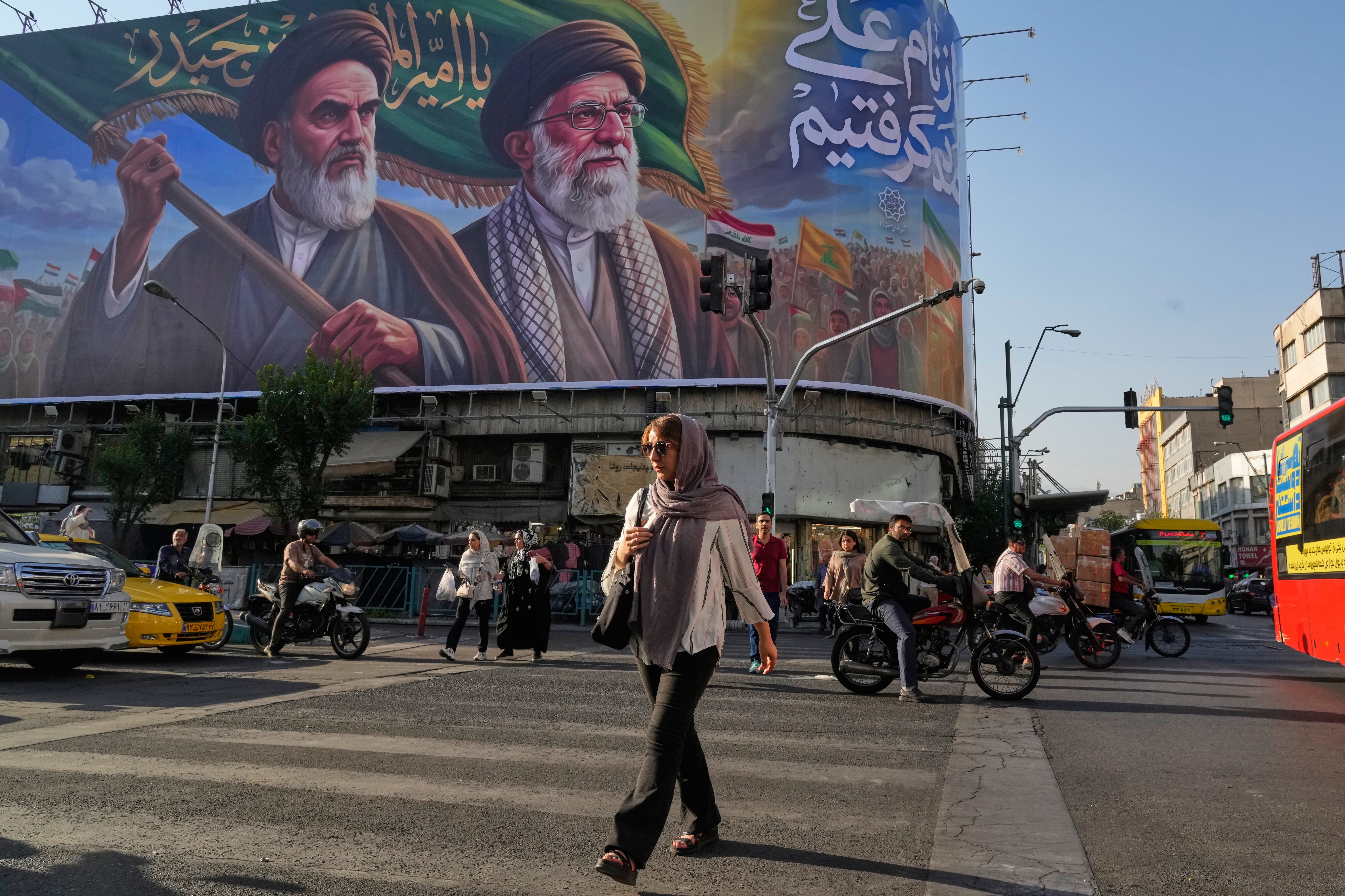 People walk under a banner showing portraits of the late revolutionary founder Ayatollah Khomeini, left, and the slain Supreme Leader Ayatollah Ali Khamenei, who was killed in U.S. and Israeli strikes on Feb. 28, in Tehran, Iran, Saturday, June 6, 2026.