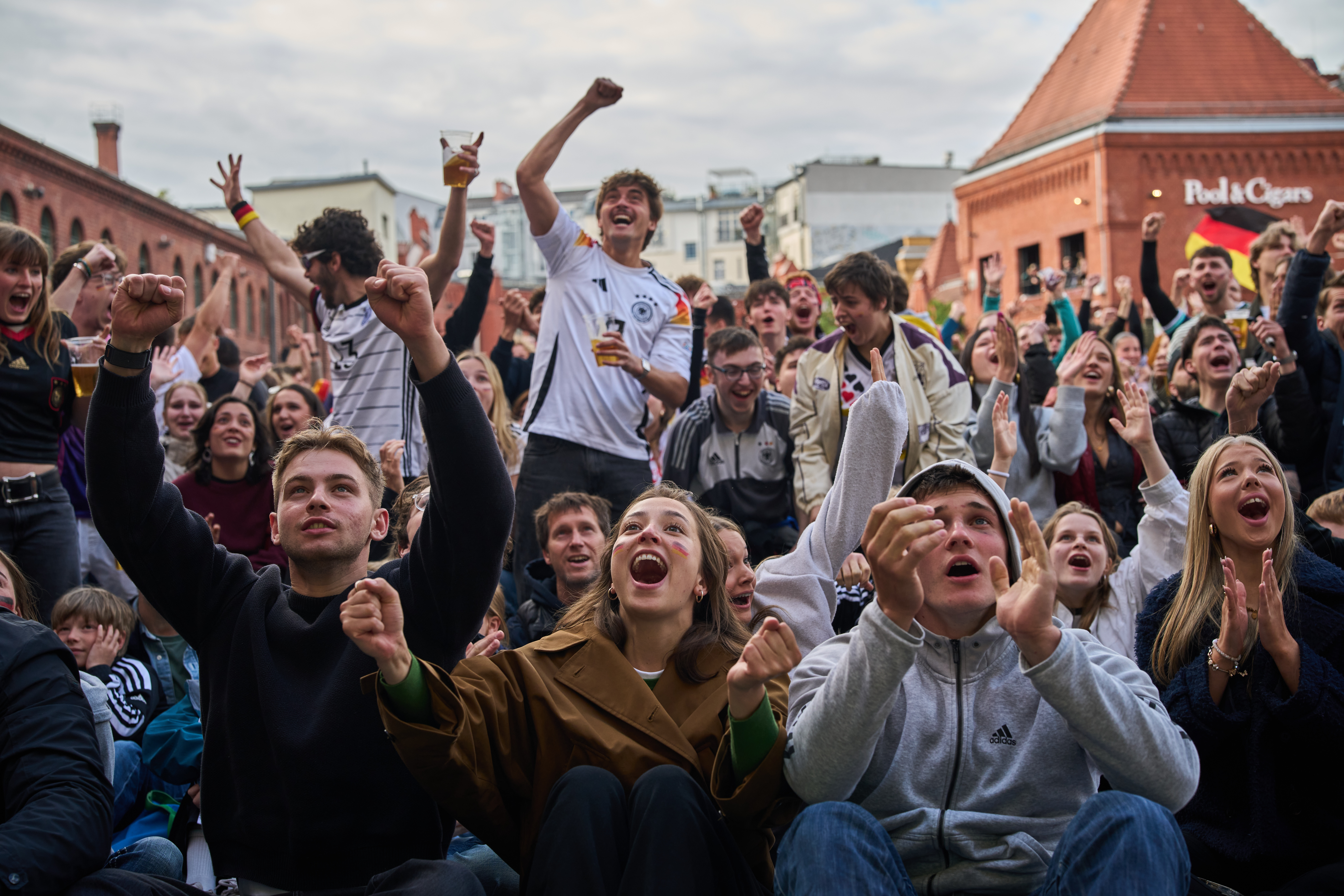Football fans cheer and celebrate their team's match in an outdoor courtyard