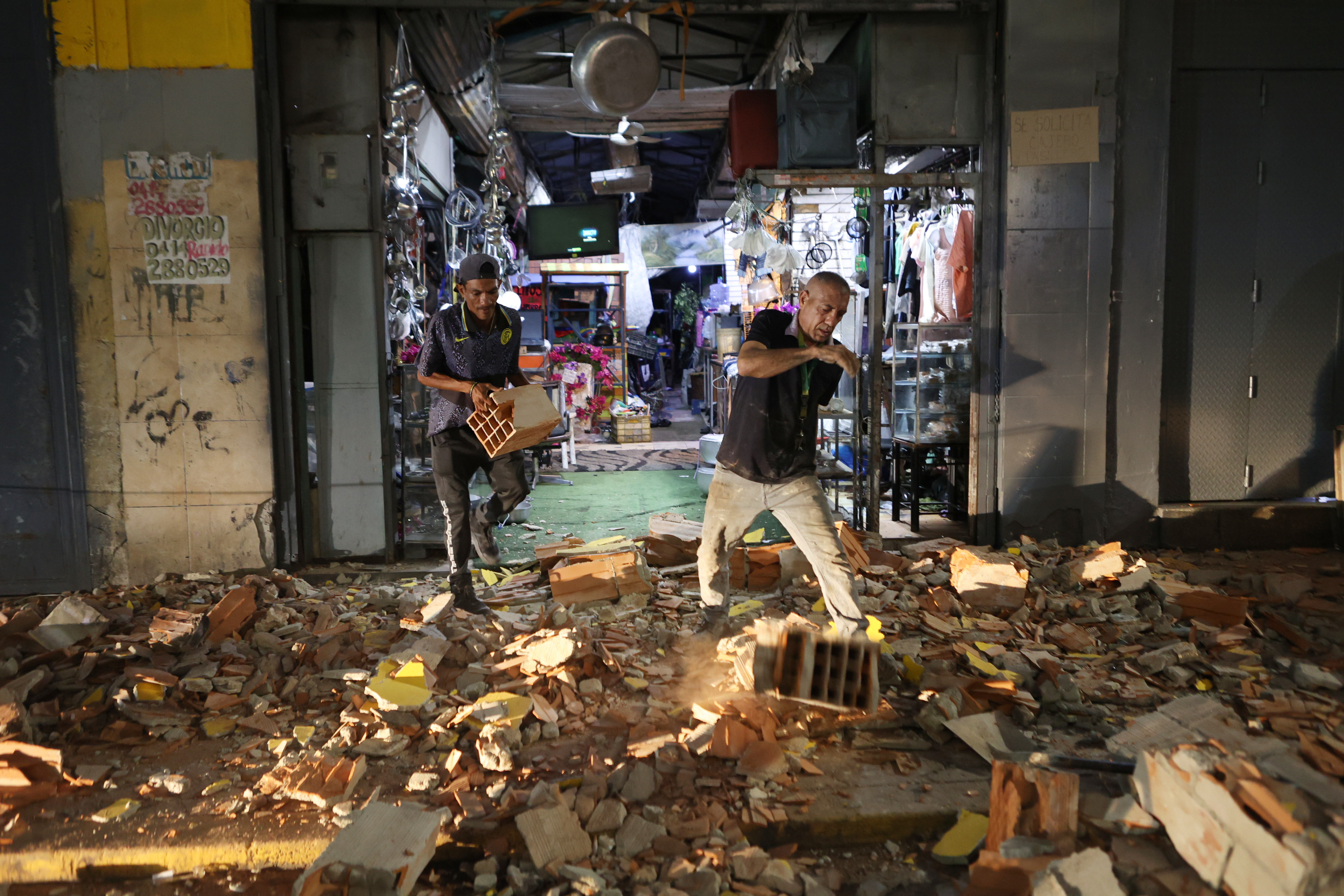 Men walk past the rubble of a collapsed building, with debris covering the street.