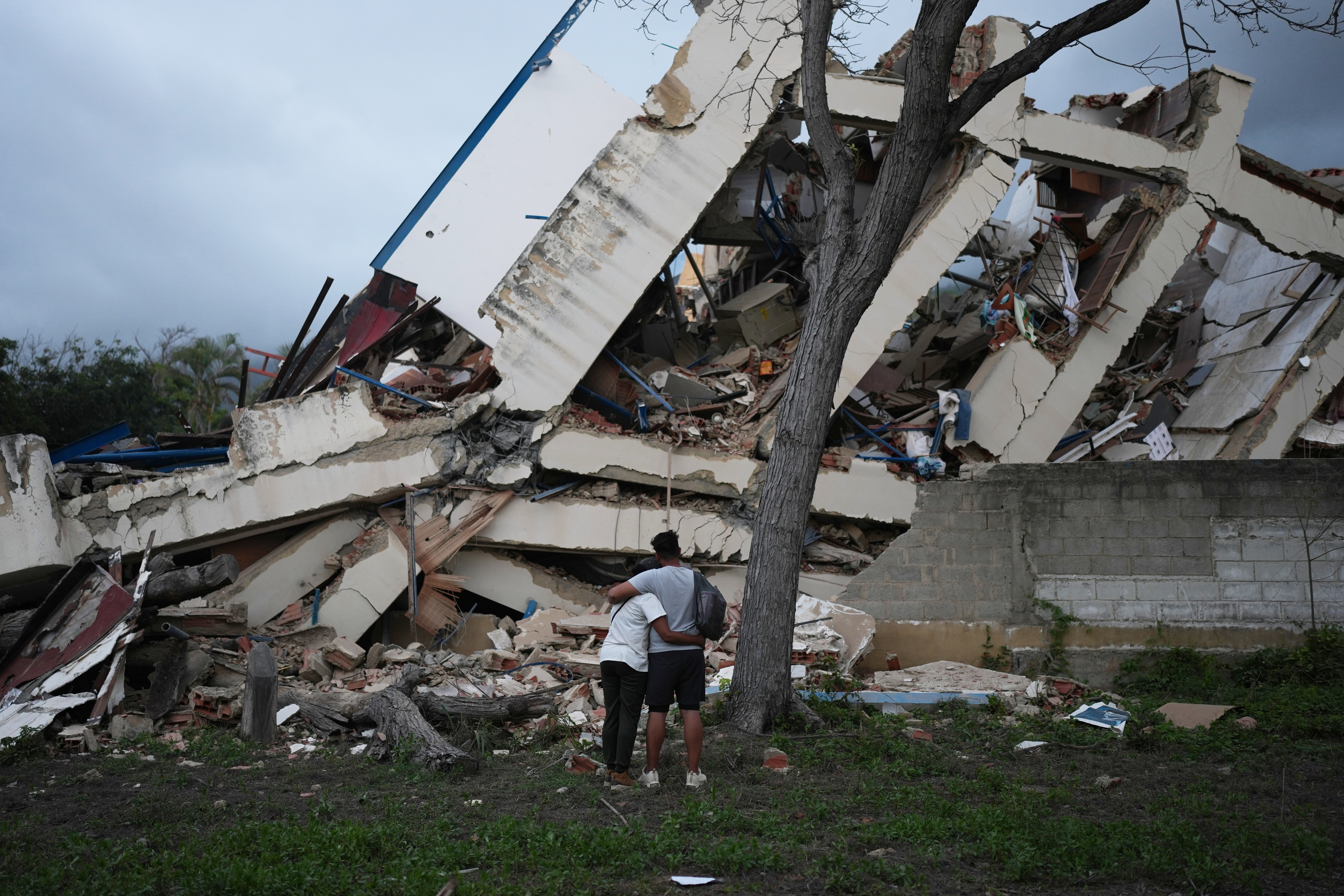 A couple embraces in front of a building destroyed by twin earthquakes three days after they struck La Guaira, Venezuela, Saturday, June 27, 2026. (AP Photo/Matias Delacroix)