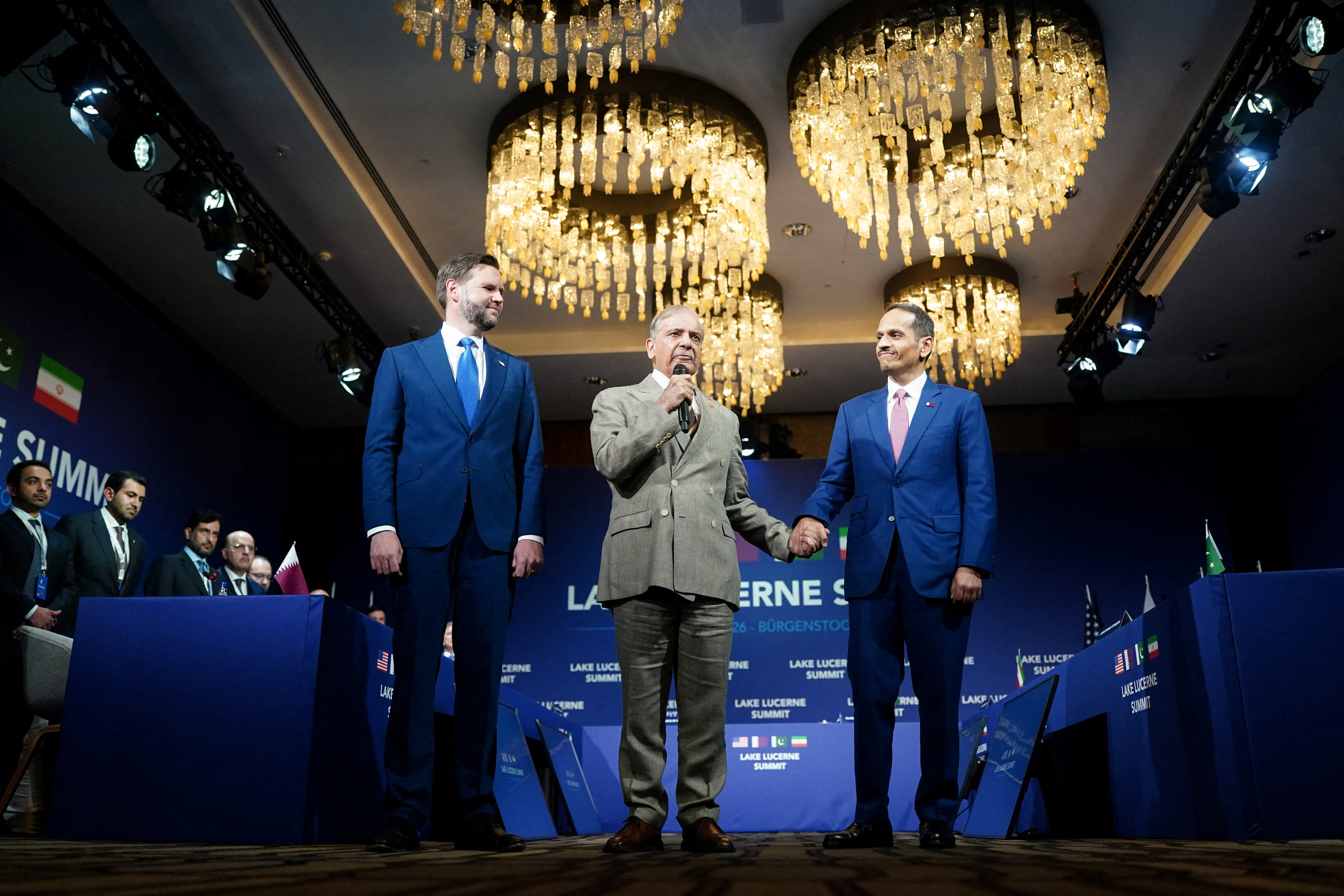 Pakistan's Prime Minister Shehbaz Sharif (C) and Qatar's Prime Minister Sheikh Mohammed bin Abdulrahman bin Jassim al-Thani hold hands next to US Vice-President JD Vance prior to a quadrilateral meeting between the United States, Iran, Pakistan and Qatar at the Burgenstock luxury hotel complex overlooking Lake Lucerne, Switzerland, on June 21, 2026, as part of high-level talks aimed at advancing a deal to end the Middle East conflict.