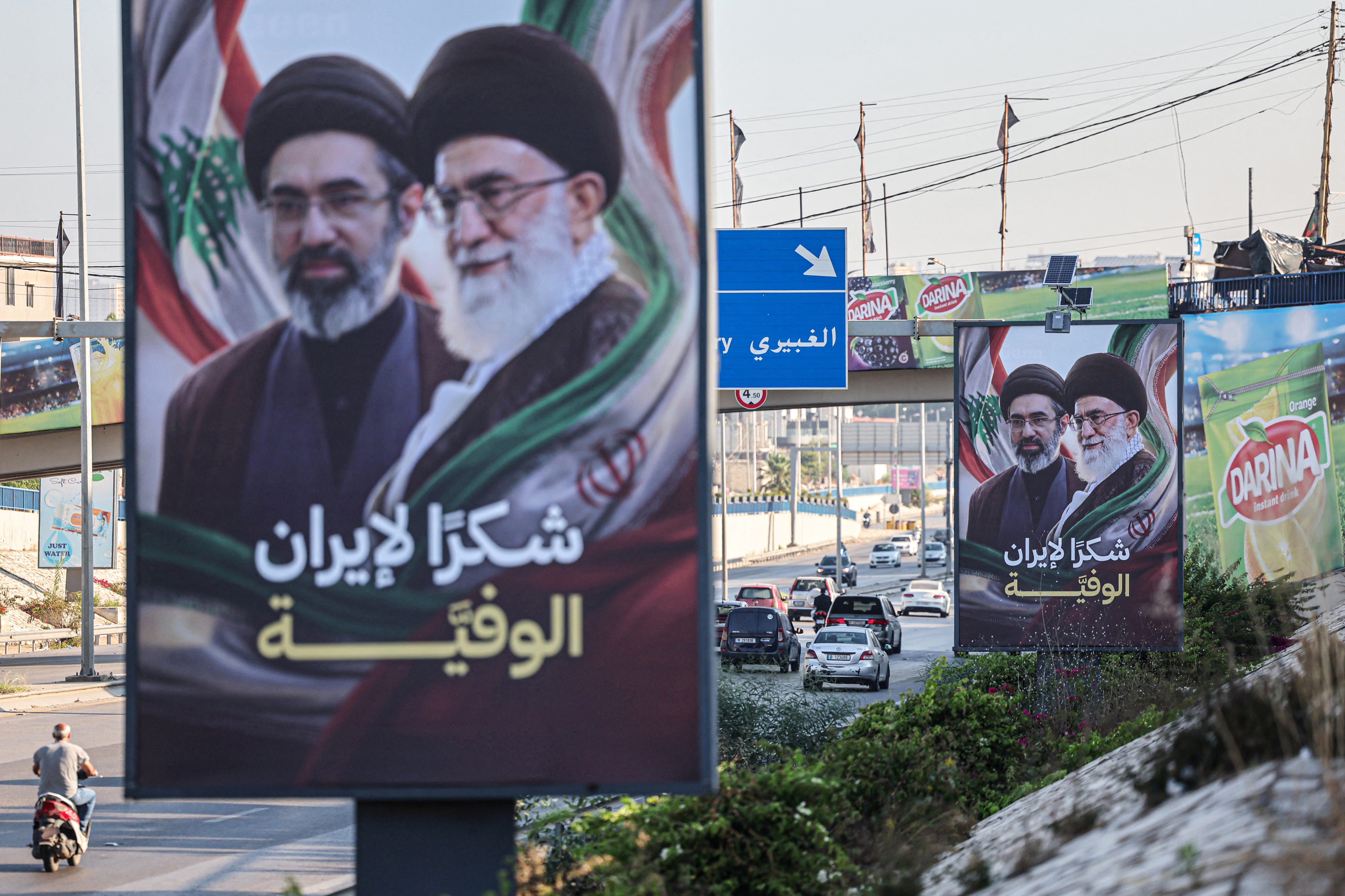 Cars and motorbikes drive past billboards showing Iran’s new Supreme Leader Ayatollah Mojtaba Khamenei (L) and his late father Ali Khamenei (R), with the slogan “Thank you, loyal Iran,” erected along the highway leading to Rafic Hariri International Airport in Beirut on June 22, 2026.