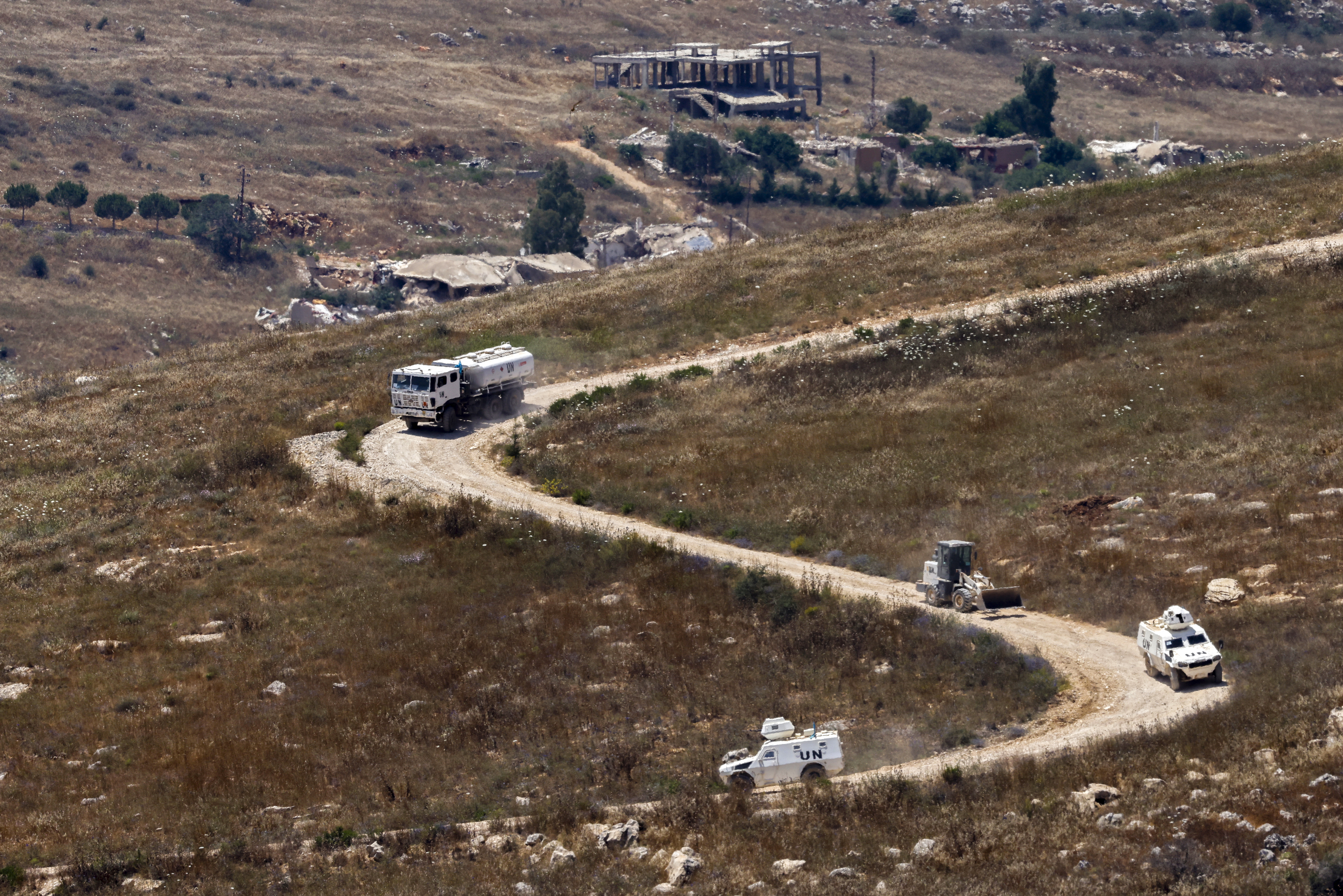 This picture taken from a position in northern Israel, near the border with Lebanon shows a United Nations Interim Force in Lebanon (UNIFIL) convoy driving past destroyed buildings in southern Lebanon on June 22, 2026.