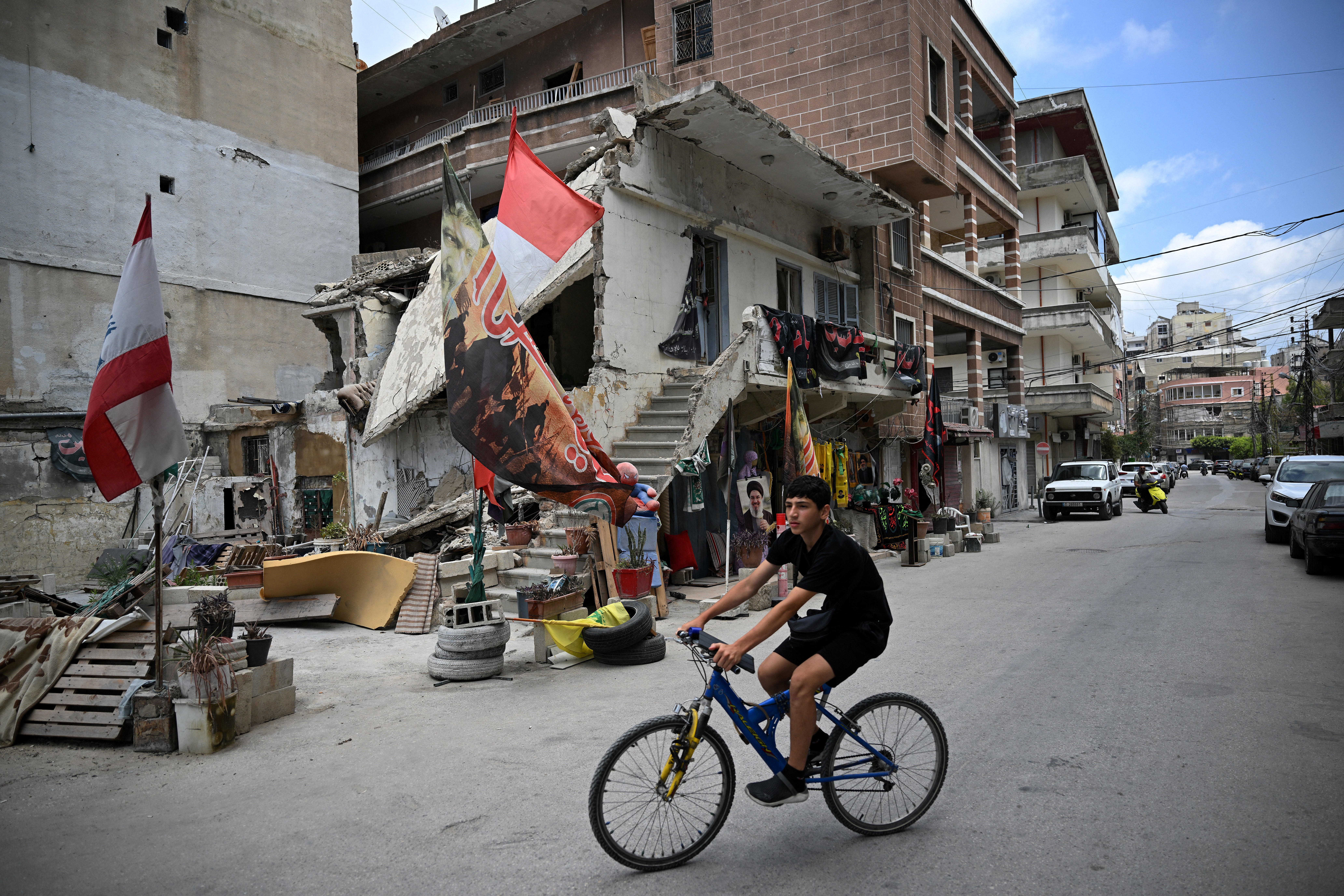 A youth rides his bike near a damaged house decorated with Shia Muslim Ashura flags as the Shia community marks the holy month of Ashura which commemorates the day one of Prophet Mohammed's grandsons was killed during a battle with unjustice King Yazid in 680 AD in Karbala of Iraq, in the southern Lebanese coastal city of Tyre on June 23, 2026.