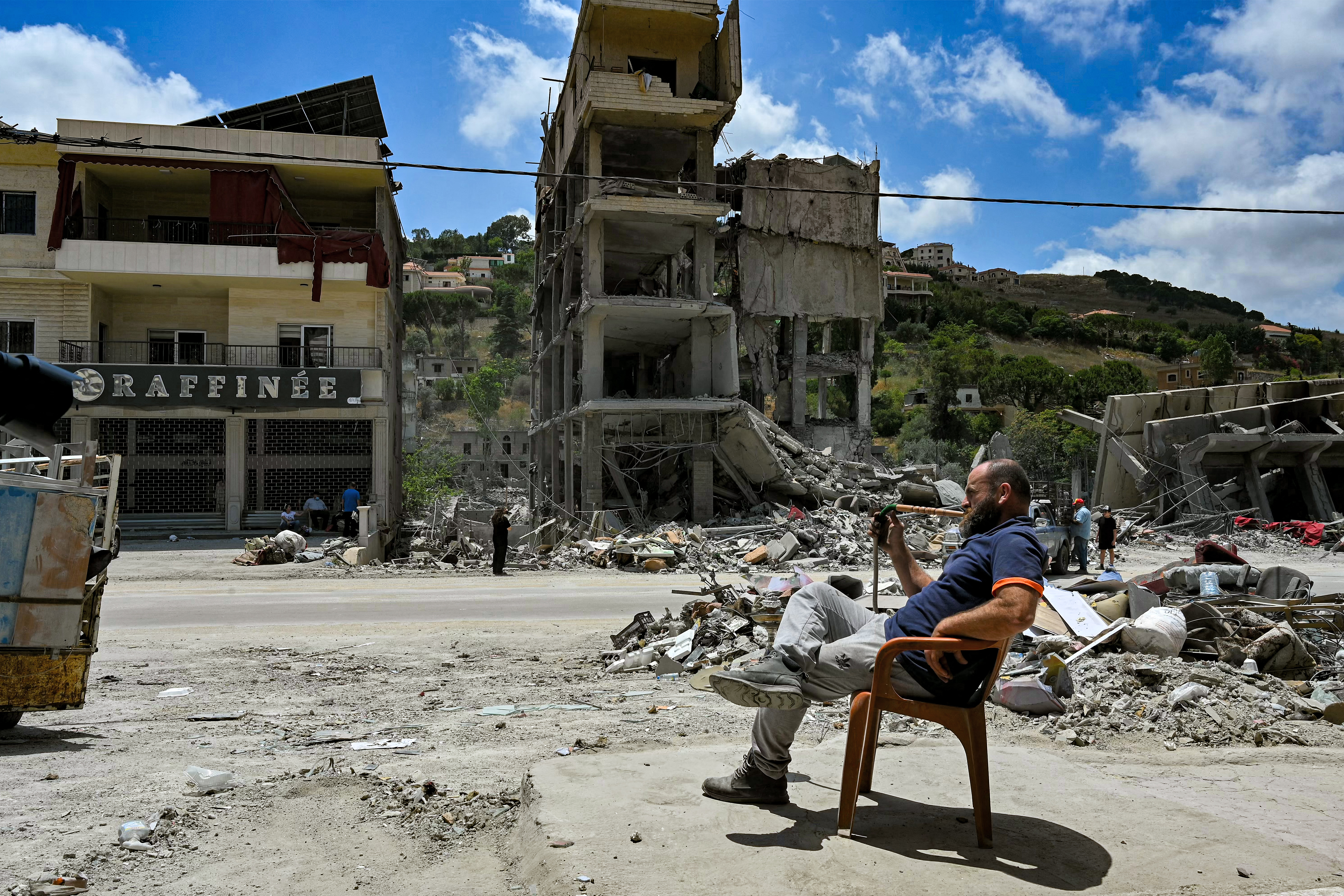 TOPSHOT - A man smokes a waterpipe as he sits by rubble in the town of Nabatieh al-Fawqa in southern Lebanon on June 23, 2026.