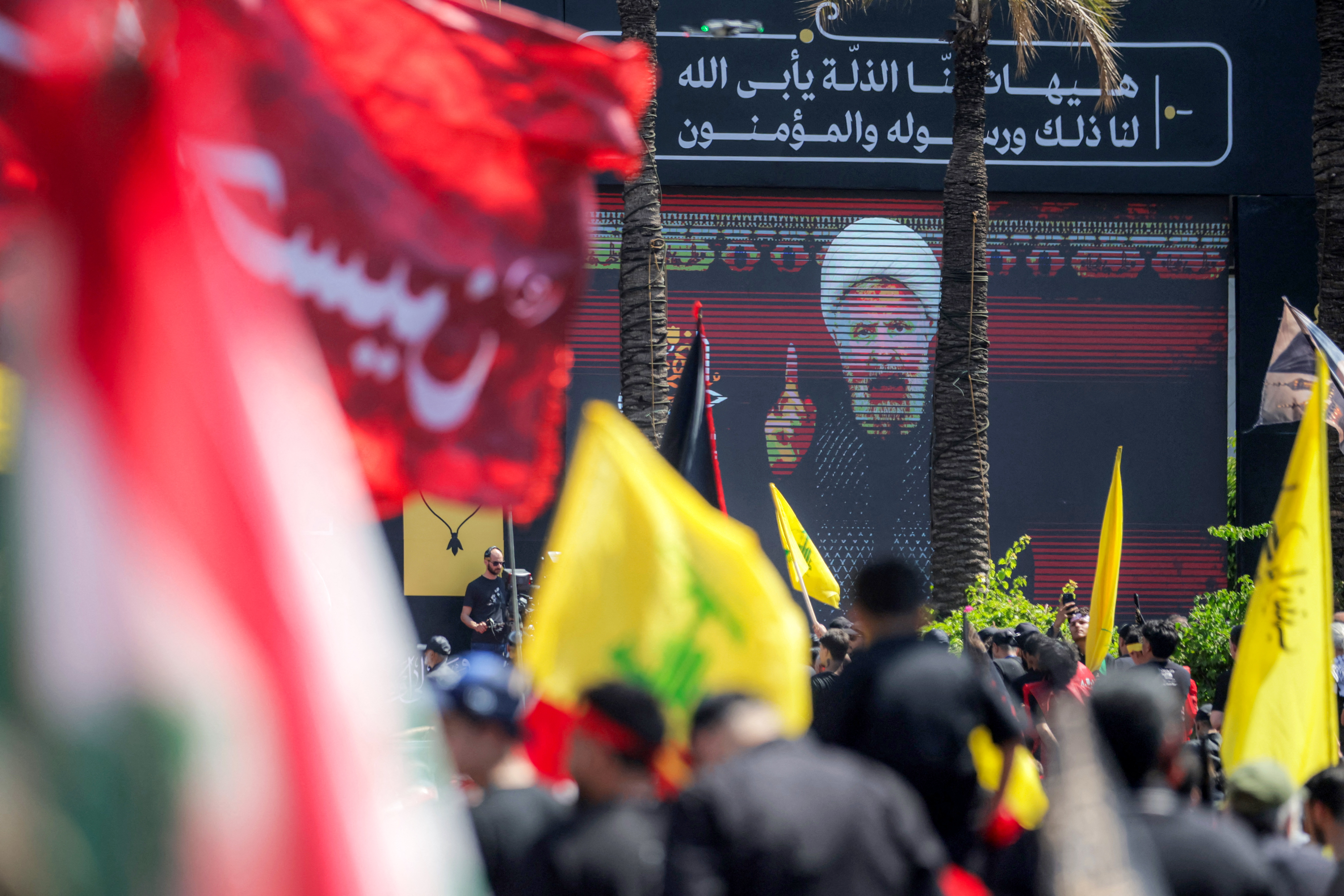 A crowd of Shia Muslim devotees watches as a televised speech by Naim Qassem, leader of Lebanese Shia movement Hezbollah, is displayed on a screen during a religious mourning event in Beirut’s southern suburbs on June 26, 2026 at the peak of Ashura, a 10-day period commemorating the seventh century killing of Prophet Mohammed's grandson Imam Hussein.
