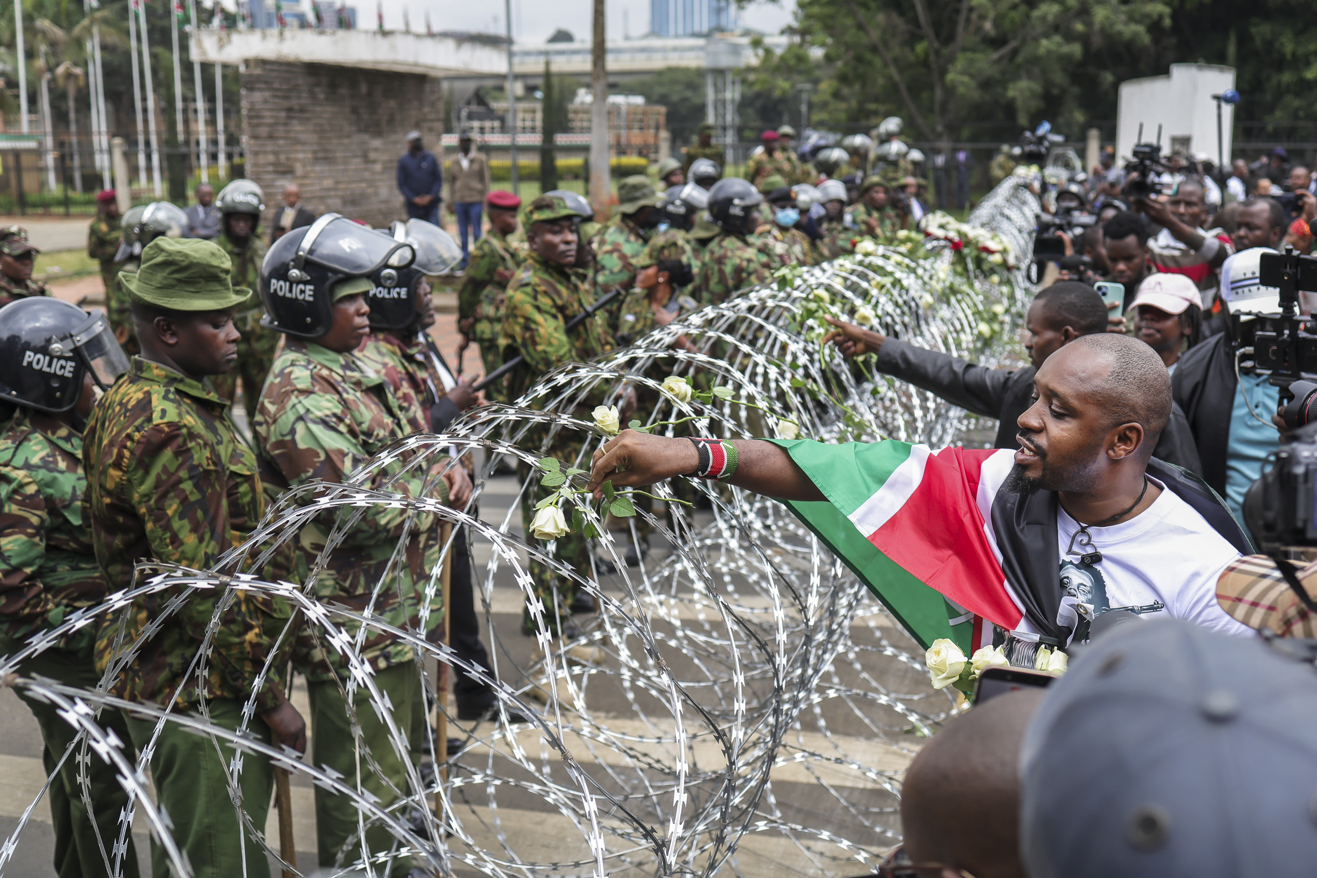 Kenyan police officers watch as activists place flowers on barbed-wire barrier set up to prevent them from gaining access to parliament precincts to lay flowers during demonstrations to mark the second anniversary of the deadly June 2024 youth-led anti-Finance Bill protests, which saw demonstrators storm Parliament, in Nairobi on June 25, 2026.