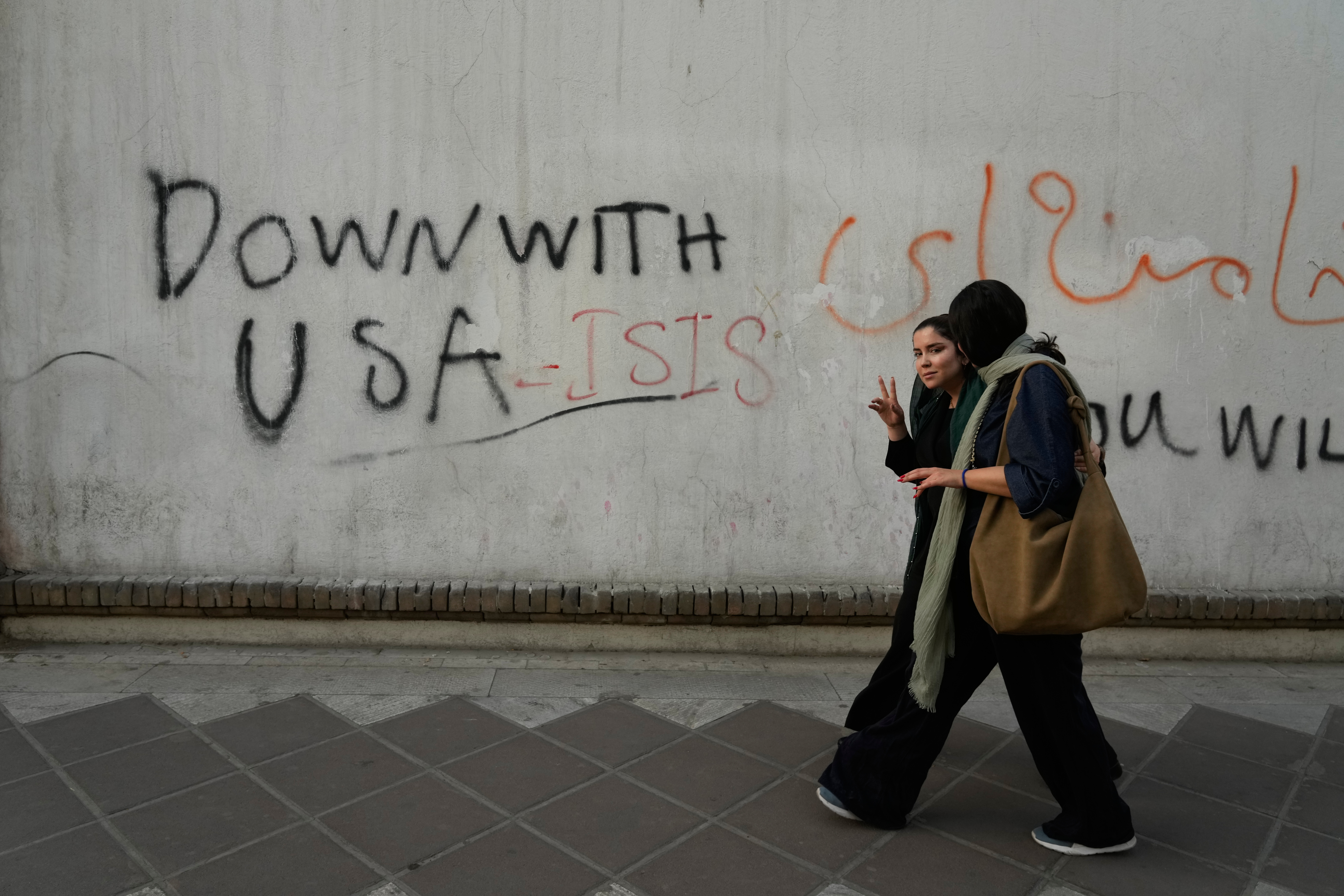 A woman makes a Victory sign to the camera as she walks past anti-US graffiti painted on a wall.