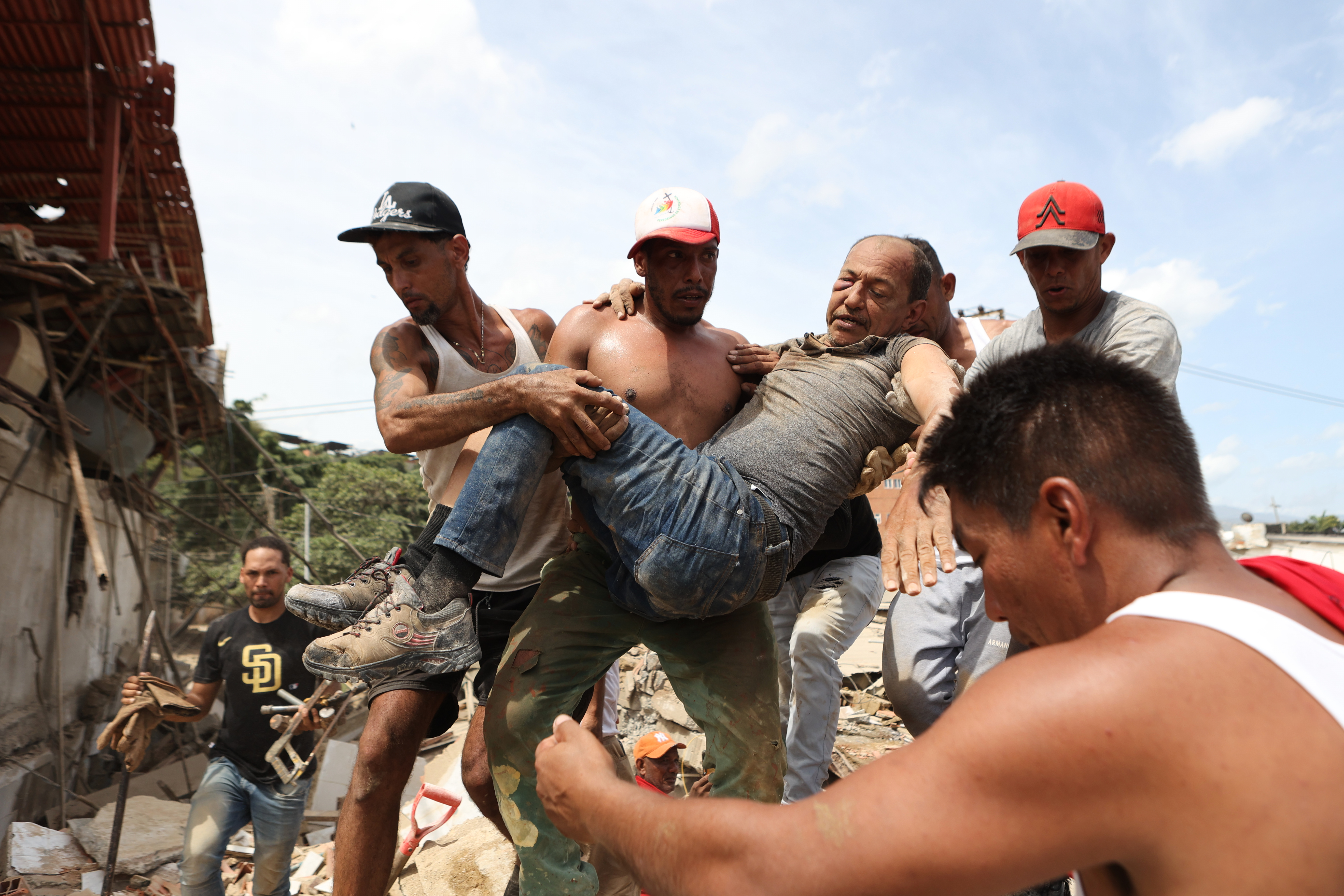 Neighbors carry a man rescued from the rubble of a collapsed building the day after earthquakes struck La Guaira, Venezuela, Thursday, June 25, 2026. (AP Photo/Pedro Mattey)