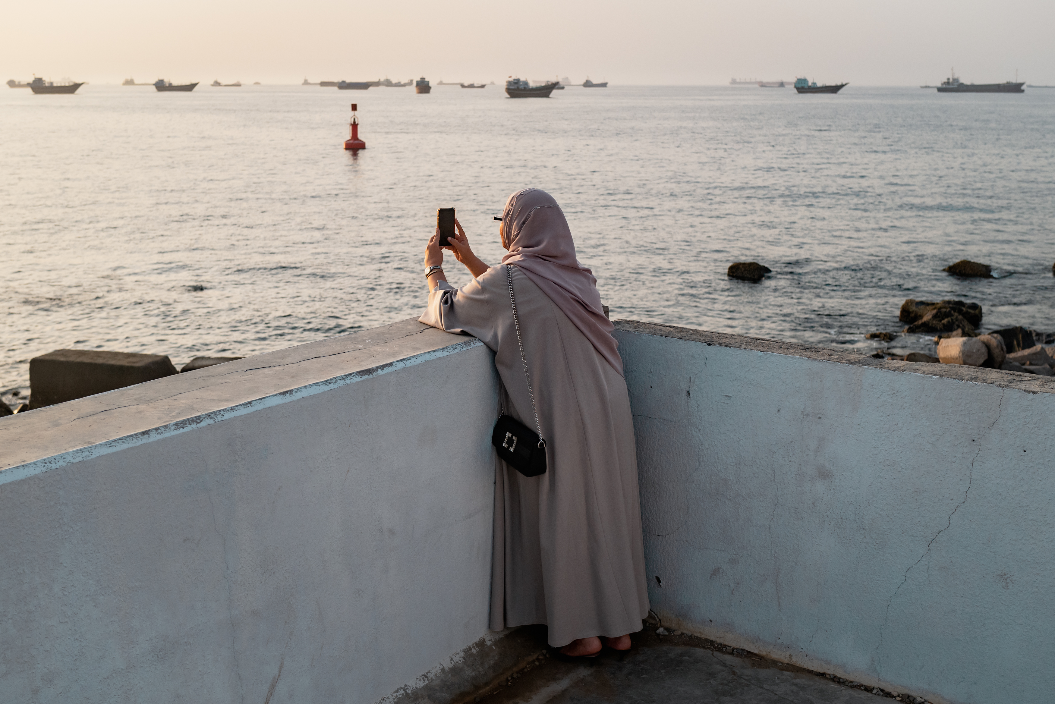 MUSCAT, OMAN - JUNE 19: An Omani woman photographs Qaboos Port where oil tankers, carriers, vessels and Omani fisherboats sit anchored on June 19, 2026 in Muscat, Oman. The port as a hub for regional trade has become a crucial maritime traffic point. The Strait of Hormuz, a vital shipping route for the region's oil and gas, was effectively blockaded since the outbreak of war between the United States and Iran in late February. This week's provisional peace deal between the countries was meant to reopen the waterway to shipping traffic, but the pace of that reopening is unclear amid continued fighting in Lebanon and the need to clear the Strait of sea mines. (Photo by Elke Scholiers/Getty Images)