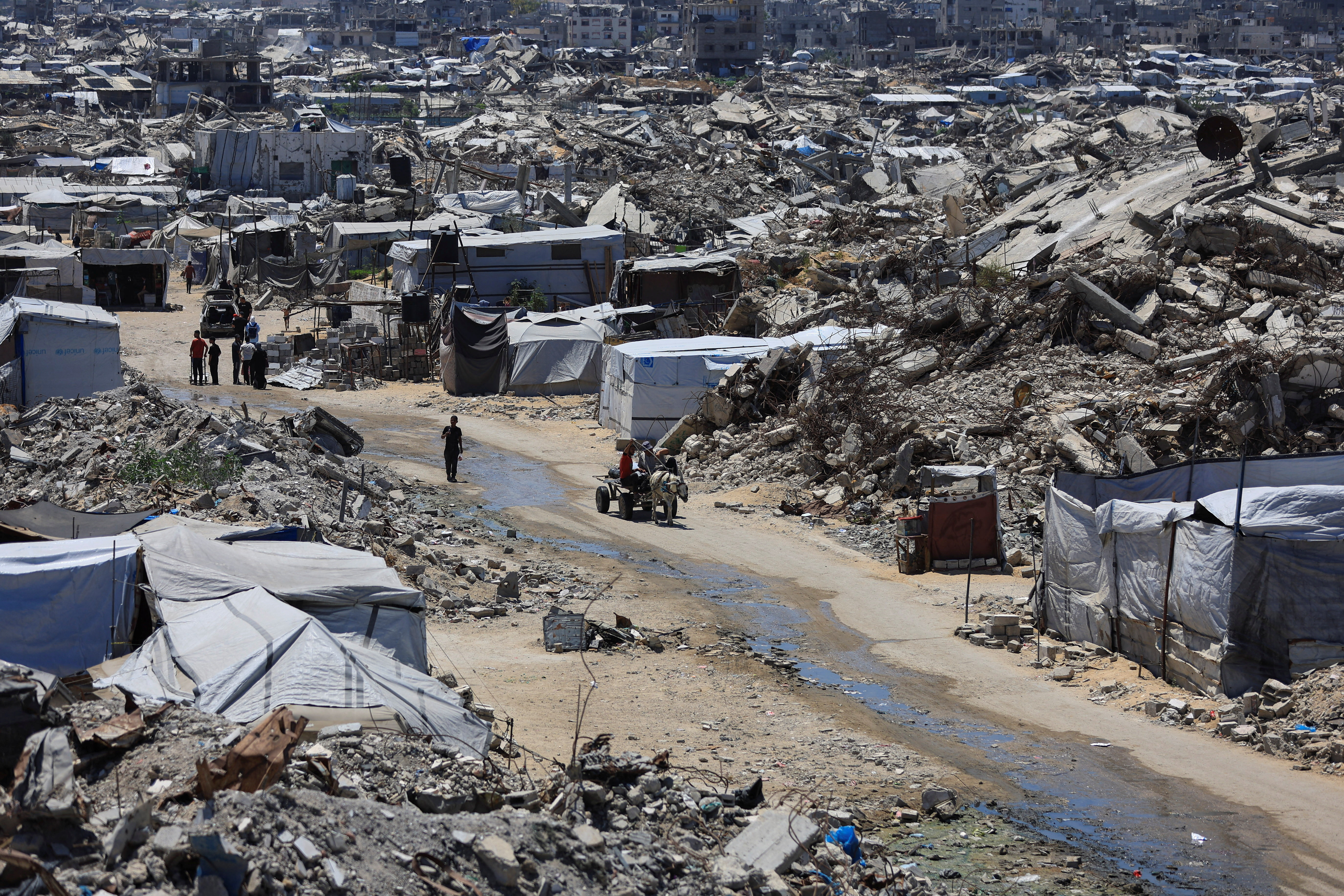 Palestinians make their way past the rubble of residential buildings destroyed during the Israeli offensive as displaced people shelter in tents, in Gaza City, June 15, 2026. REUTERS/Dawoud Abu Alkas
