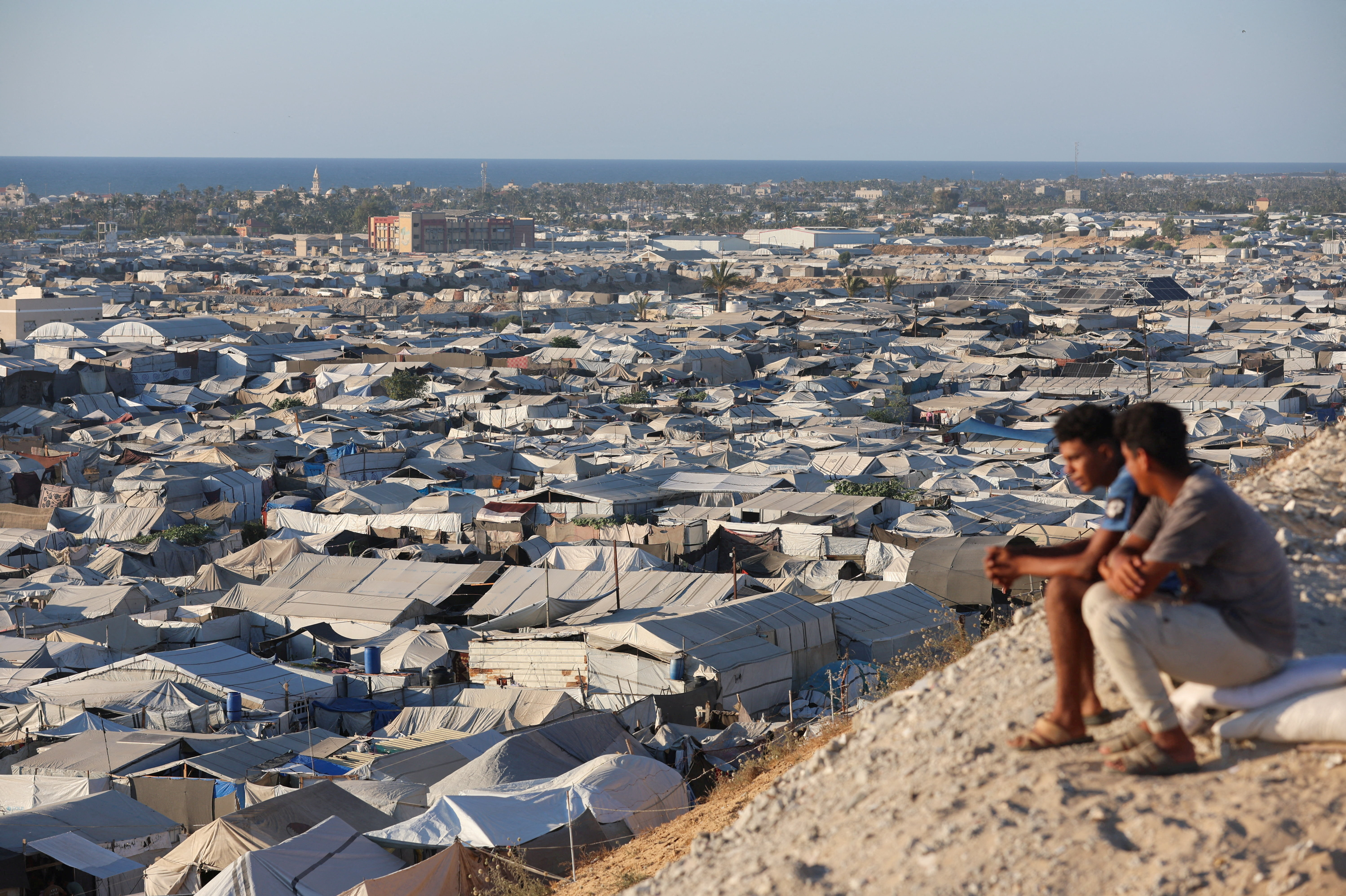 Palestinians sit overlooking a tent camp sheltering displaced people, in Khan Younis in the southern Gaza Strip, June 18, 2026. REUTERS/Ramadan Abed TPX IMAGES OF THE DAY