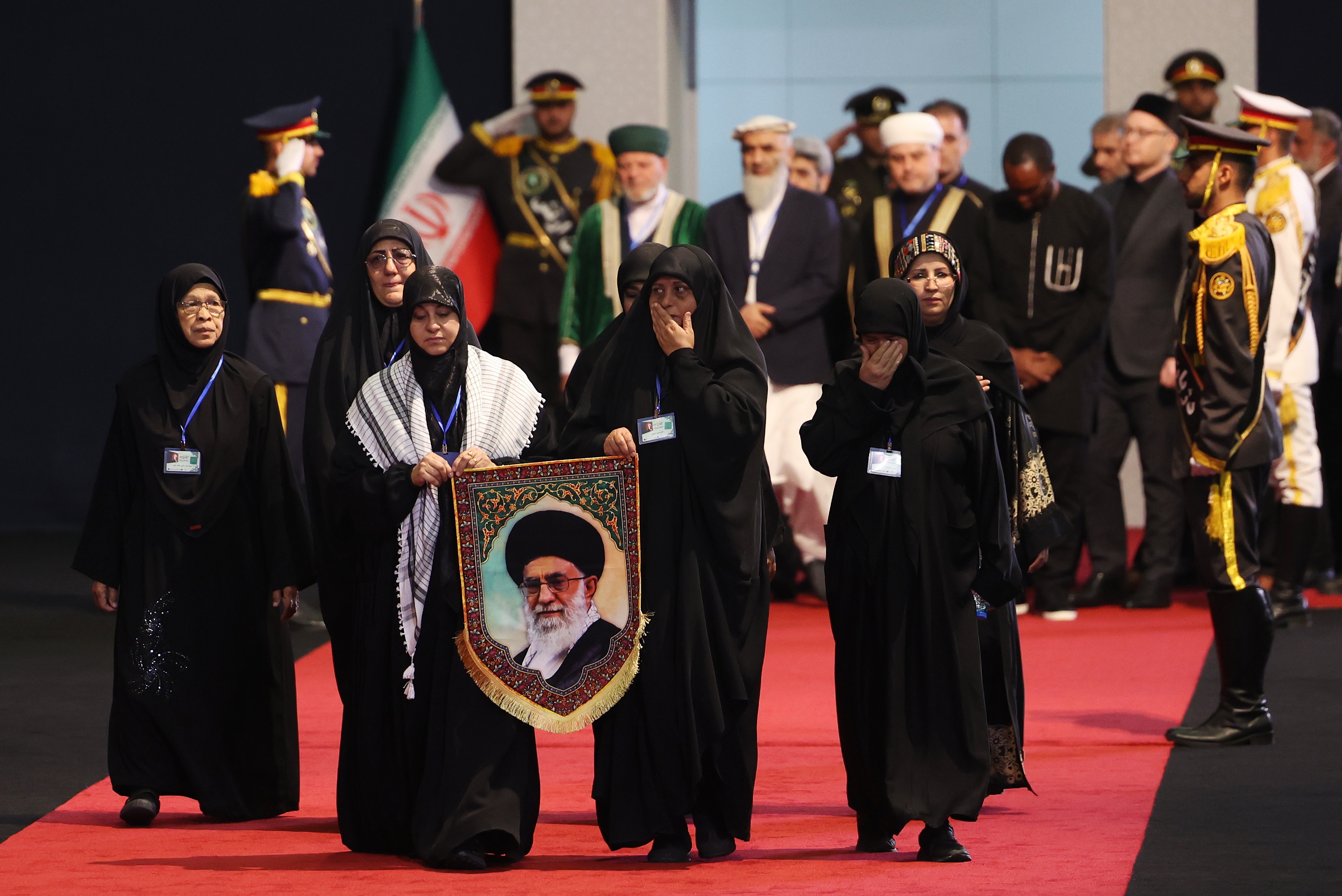 Women holding a portrait of late Iranian Supreme Leader Ayatollah Ali Khamenei pay their respects.