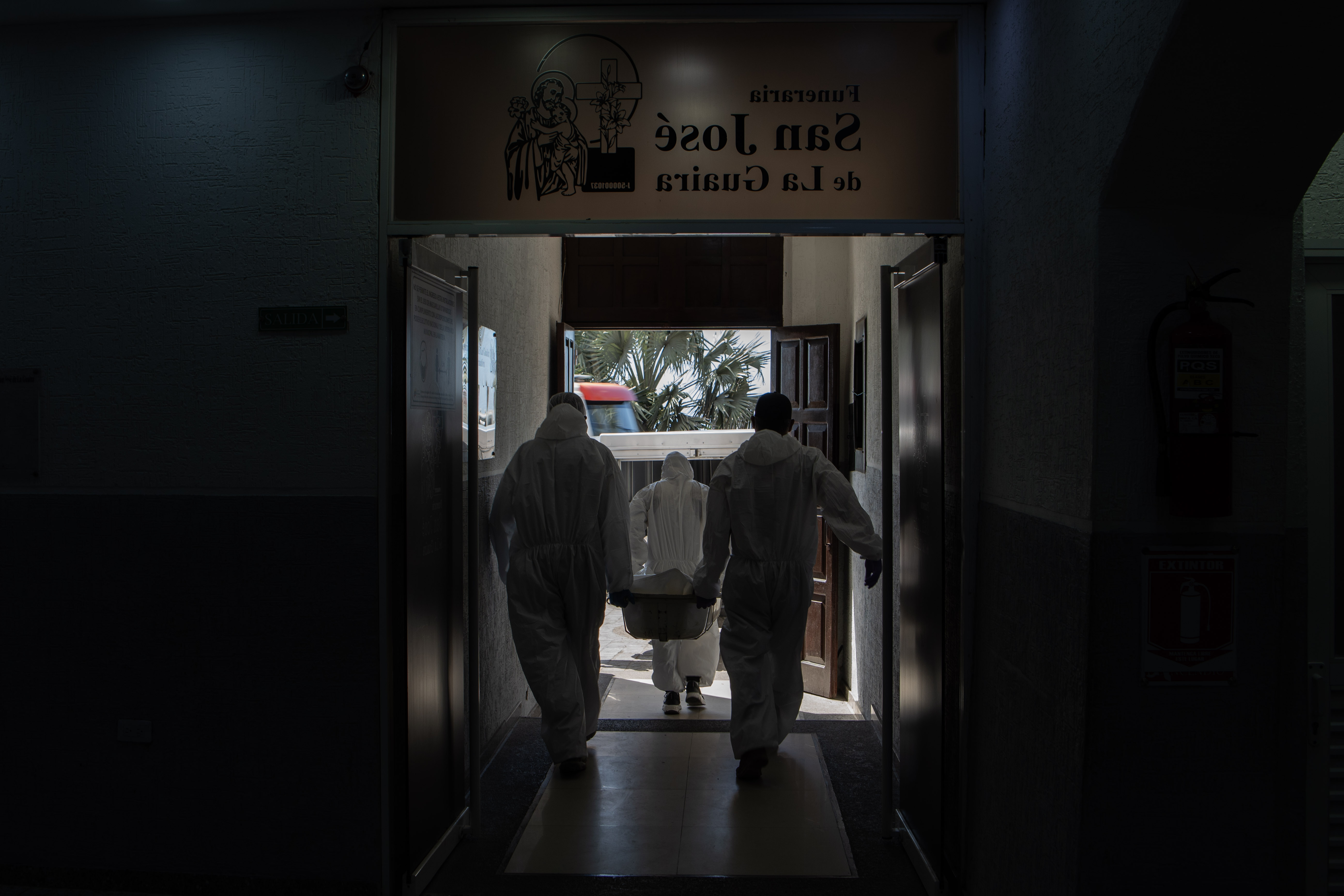 Workers in white forensic overalls lug corpses out of the building and stack them in a van