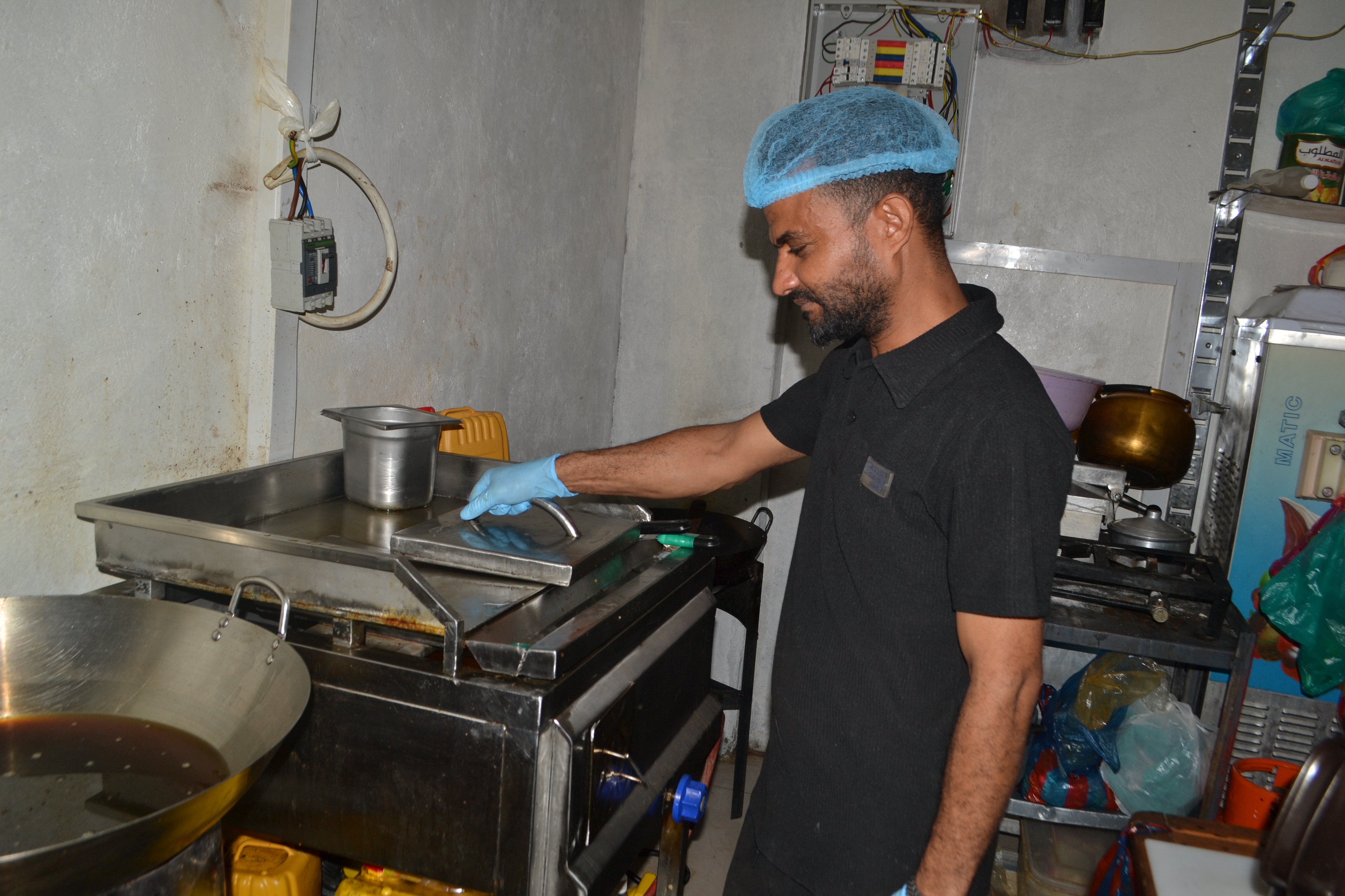 Baleegh Al-Doba’ai works as the head chef in the kitchen of Abu Sultan, a fast-food restaurant managed by his wife. [Nasser Al-Sakkaf/Al Jazeera]
