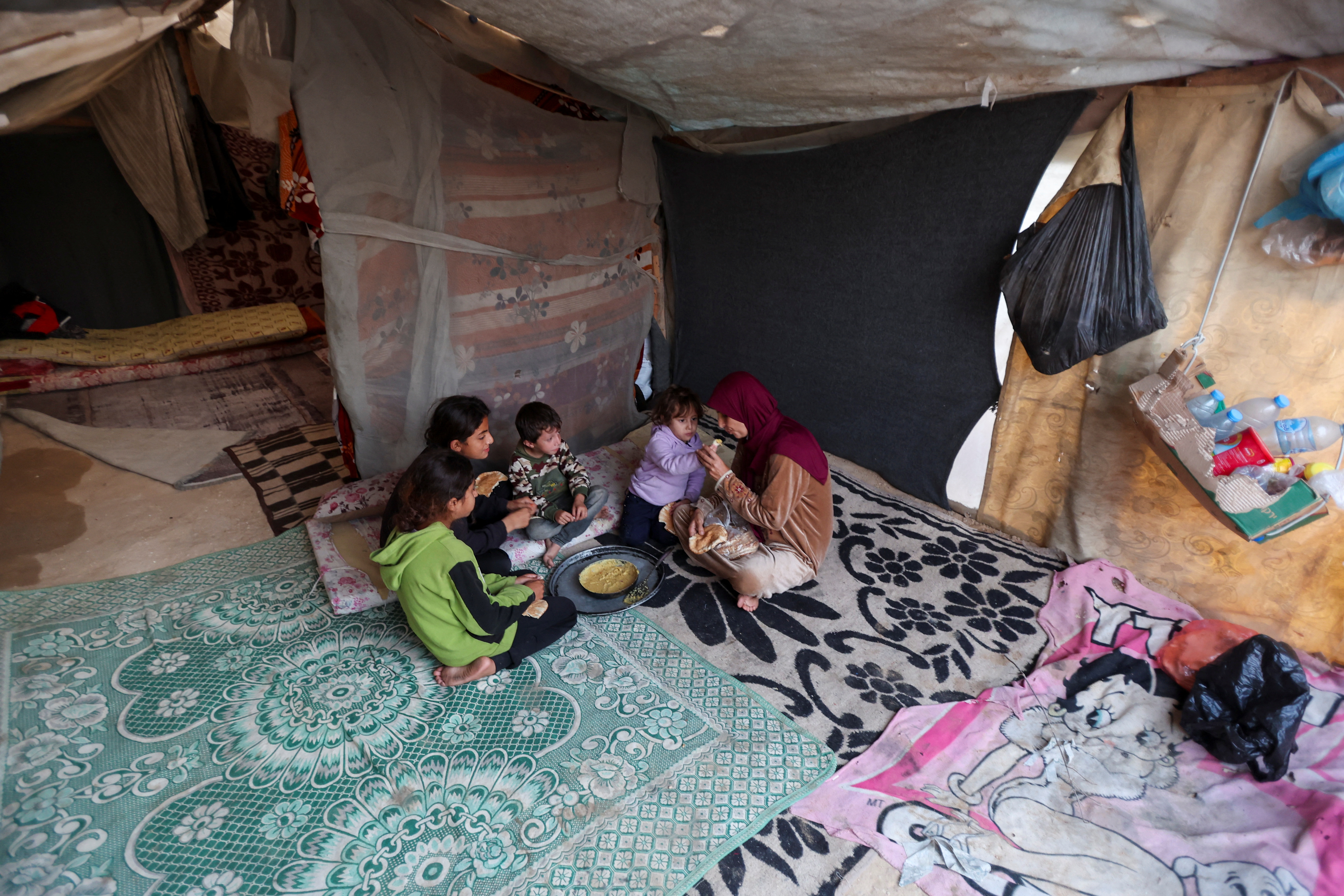 A displaced Palestinian mother has a meal with her children inside a tent in Deir el-Balah. The war has led to malnutrition and psychological strain, which has taken a particular toll on pregnant women