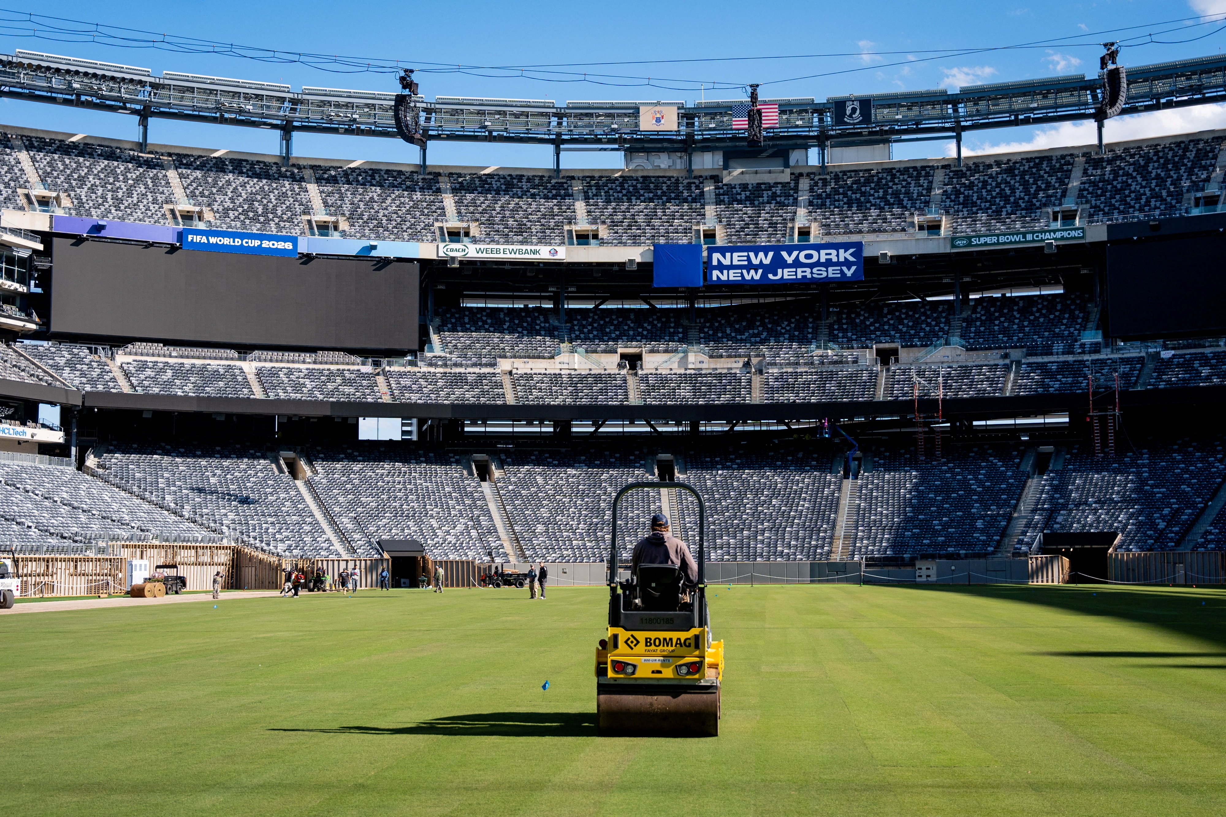 Workers lay rolls of turf across the floor of a vast empty stadium