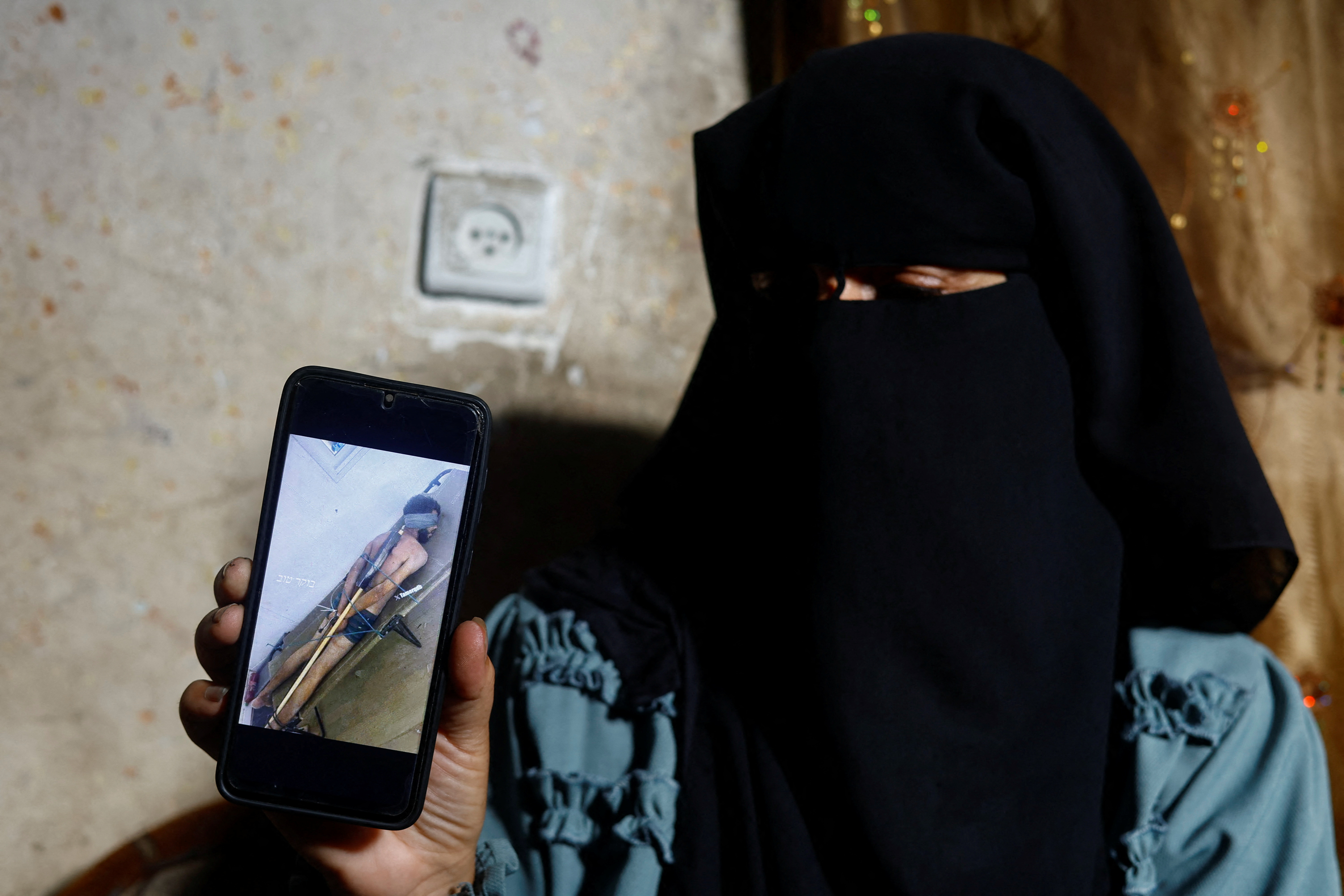 Rana Abu Nassar, mother of Palestinian prisoner Osama Abu Nassar who is held by Israel, holds a mobile phone displaying a widely circulated image that she believes shows her son restrained while in Israeli custody, at her home in Al-Maghazi refugee camp, central Gaza Strip, July 3, 2026. The image has sparked a desperate search for the man's identity, with two Palestinian families claiming him as their son. REUTERS/Mahmoud Issa