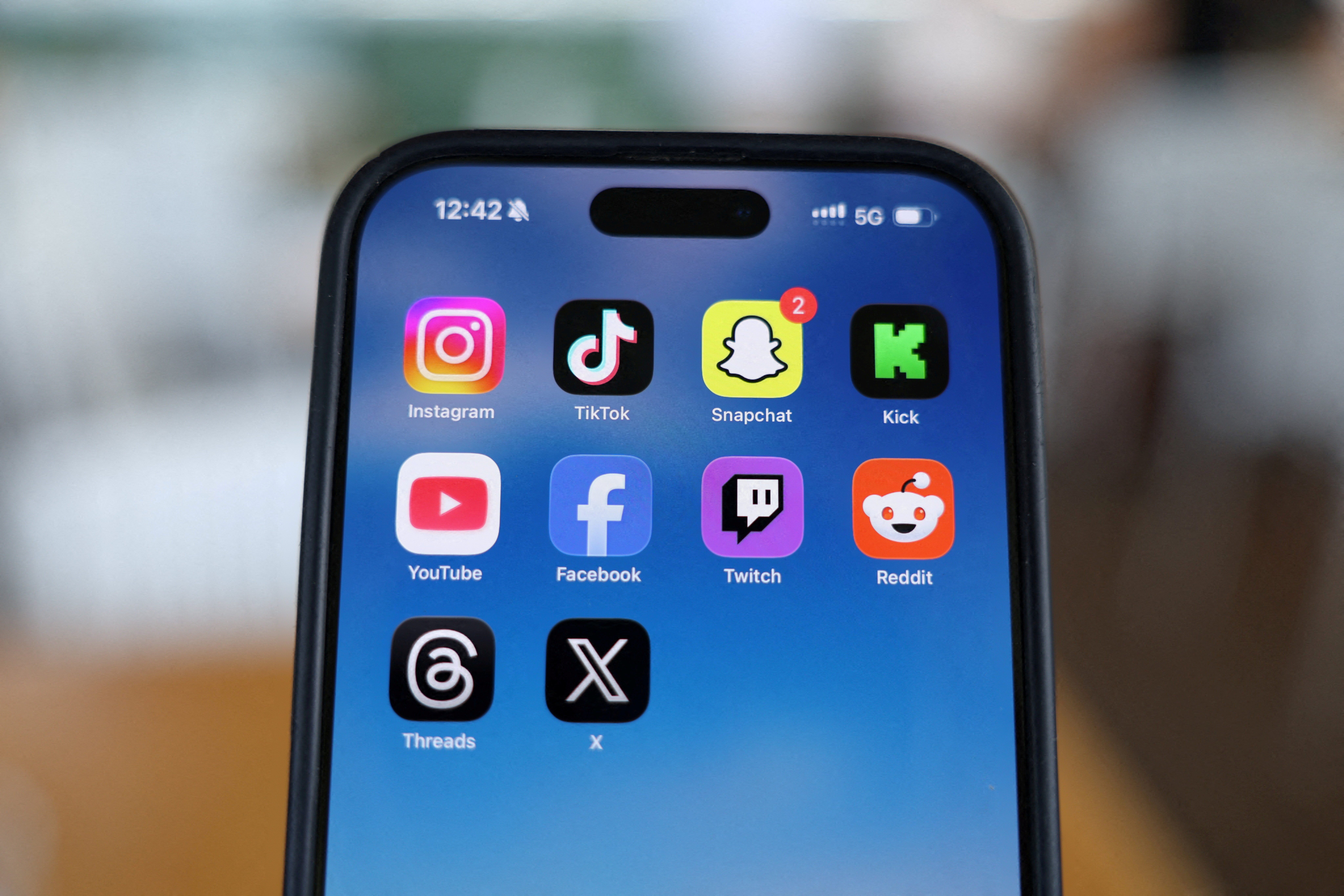 Instagram, TikTok, Snapchat, Kick, YouTube, Facebook, Twitch, Reddit, Threads and X applications are displayed on a mobile phone. [File: Hollie Adams/Reuters]