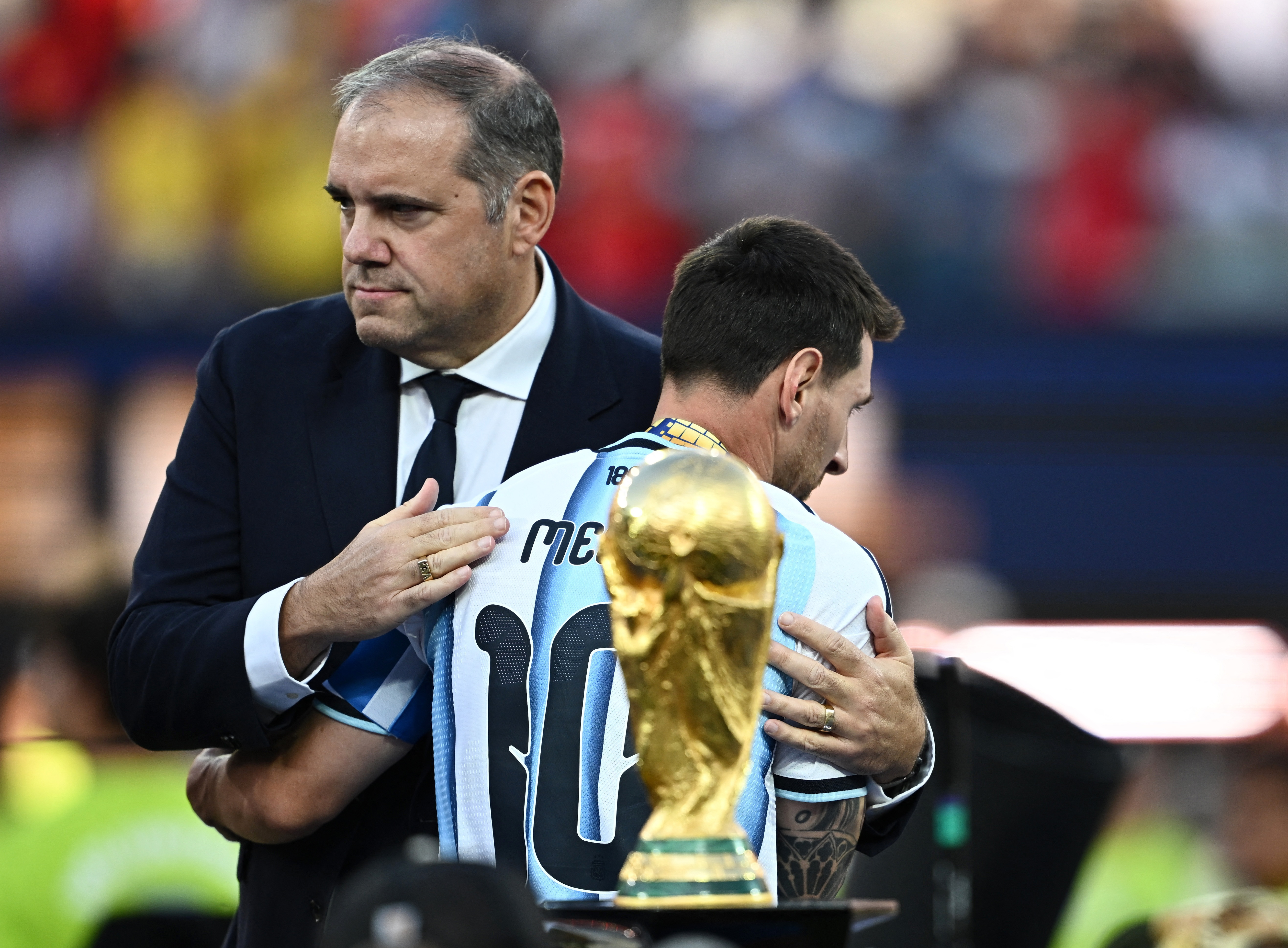 The World Cup trophy is seen as Argentina's Lionel Messi embraces CONCACAF President Victor Montagliani.