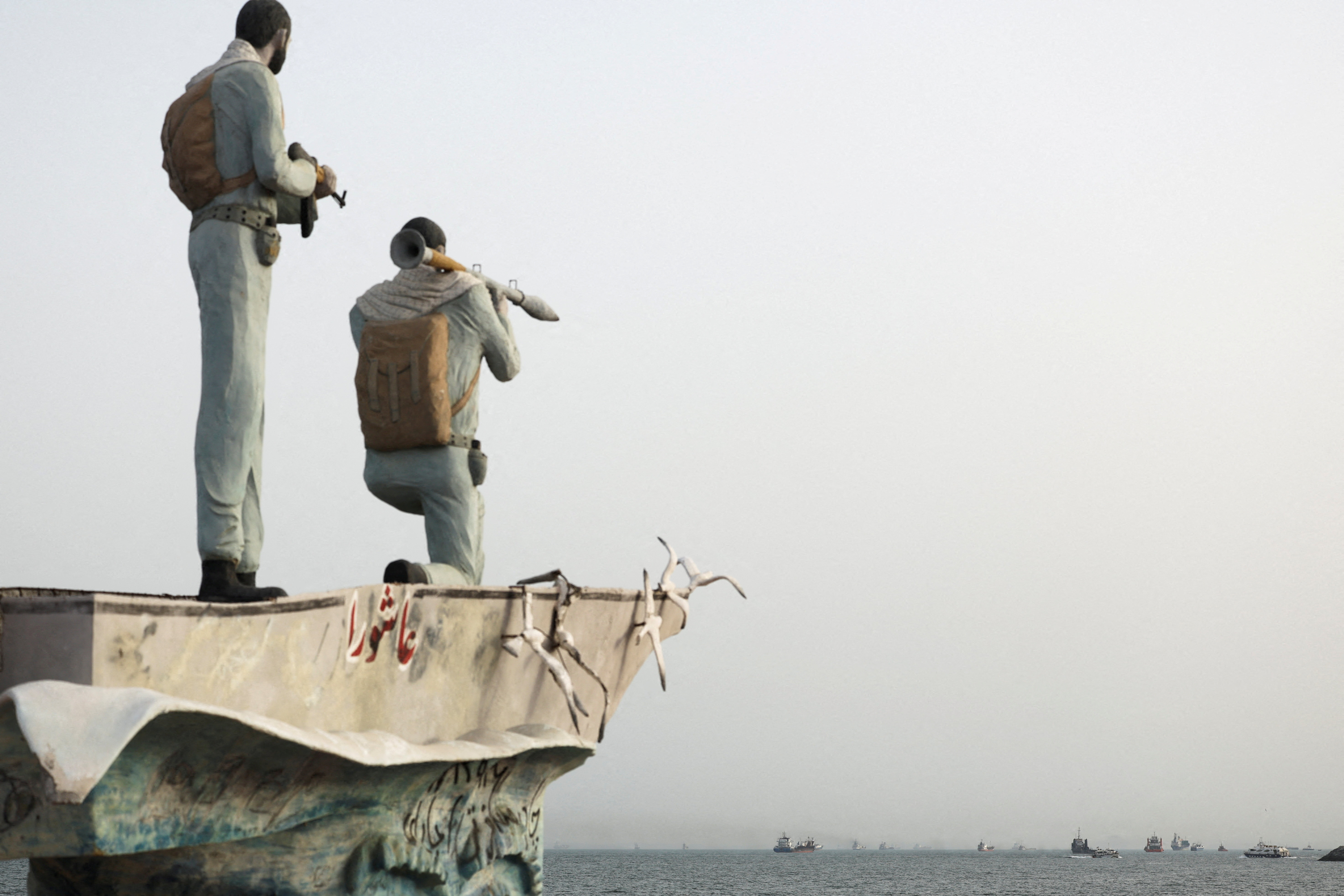 statue of Iranian military members stands as vessels in the Strait of Hormuz are visible near the beach of Bandar Abbas, Iran, May 22, 2026.