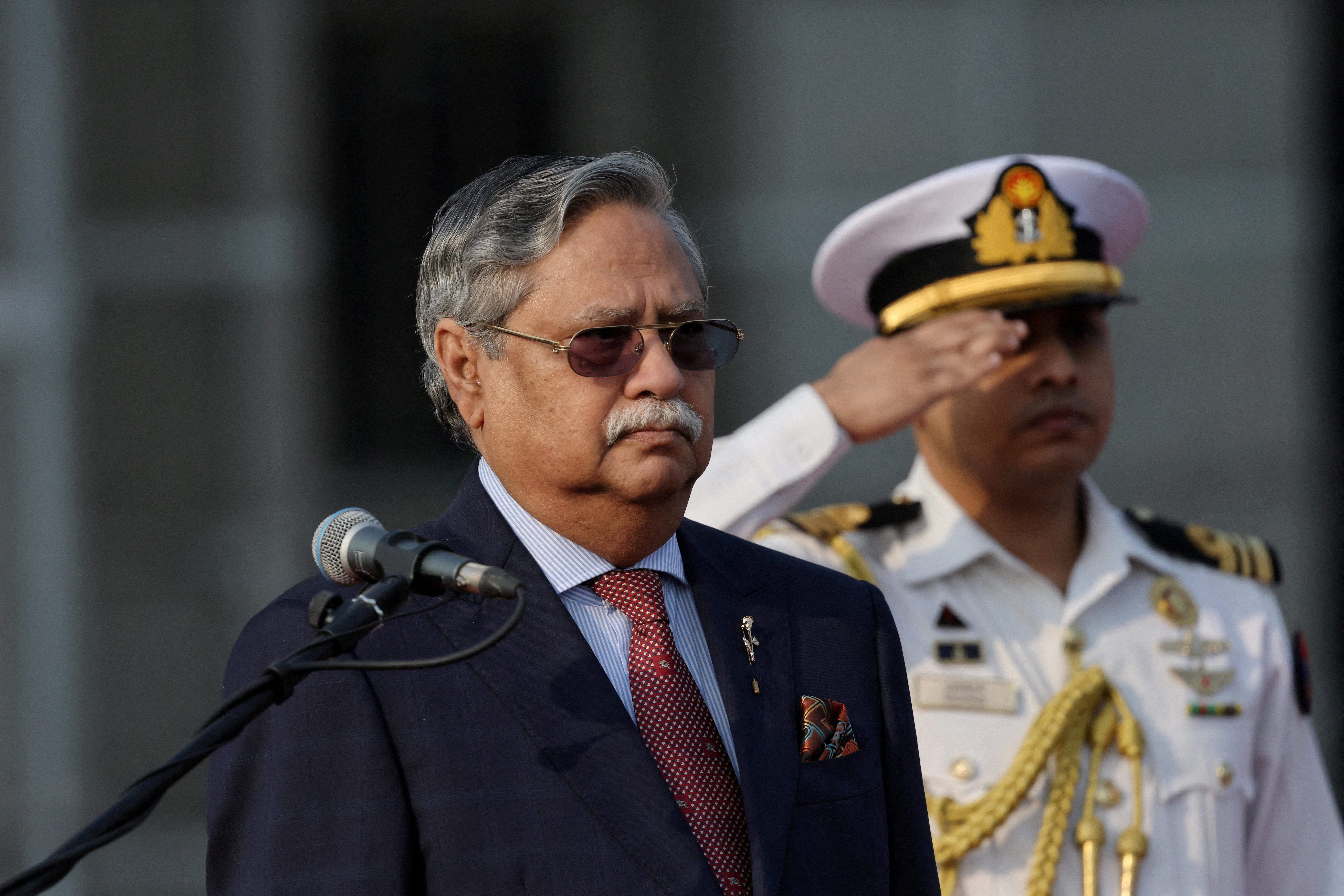 A man in a suit stands near a uniformed officer