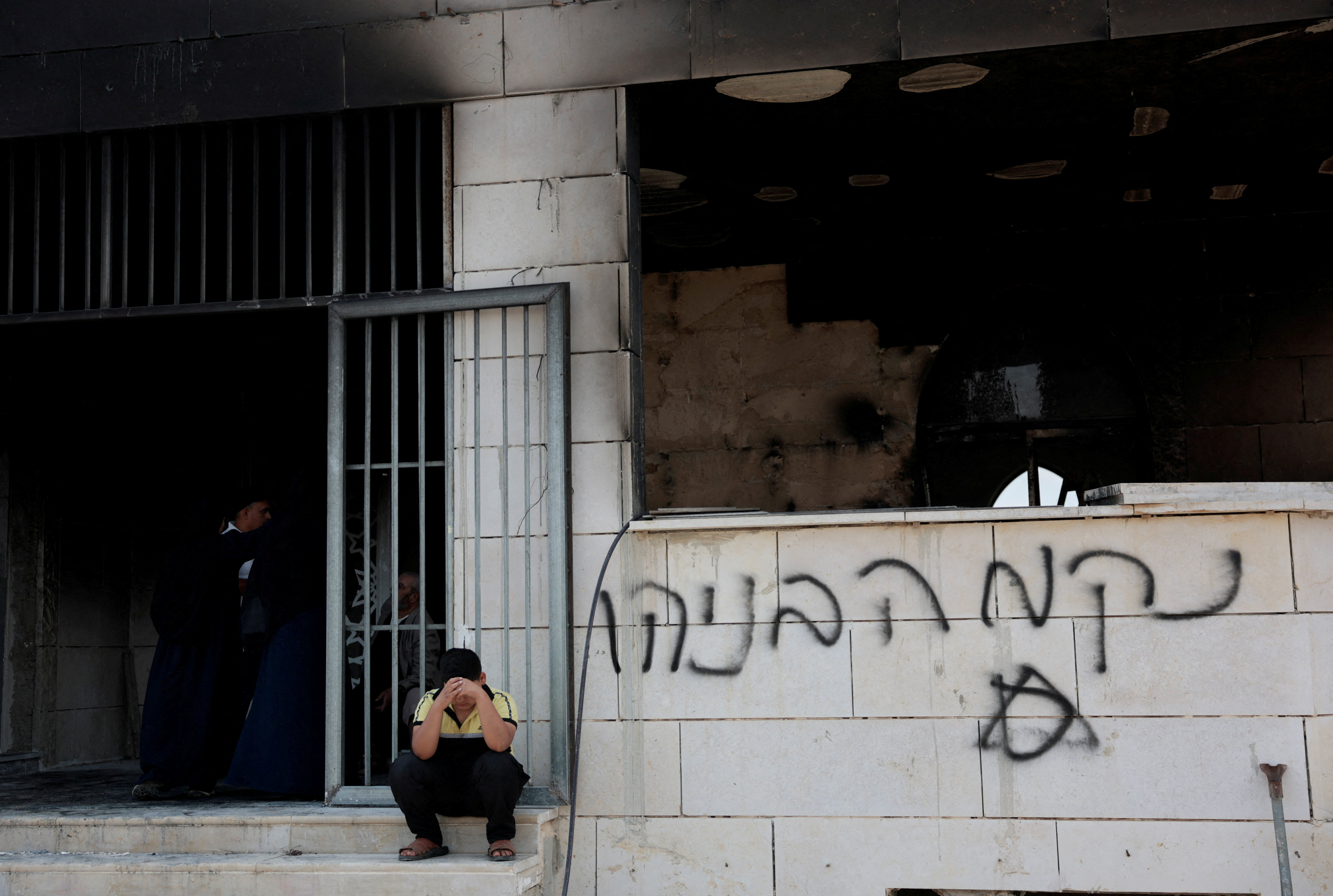 A Palestinian boy sits outside a mosque damaged by Israeli settlers, in Qusra near Nablus, in the Israeli-occupied West Bank, July 26, 2026