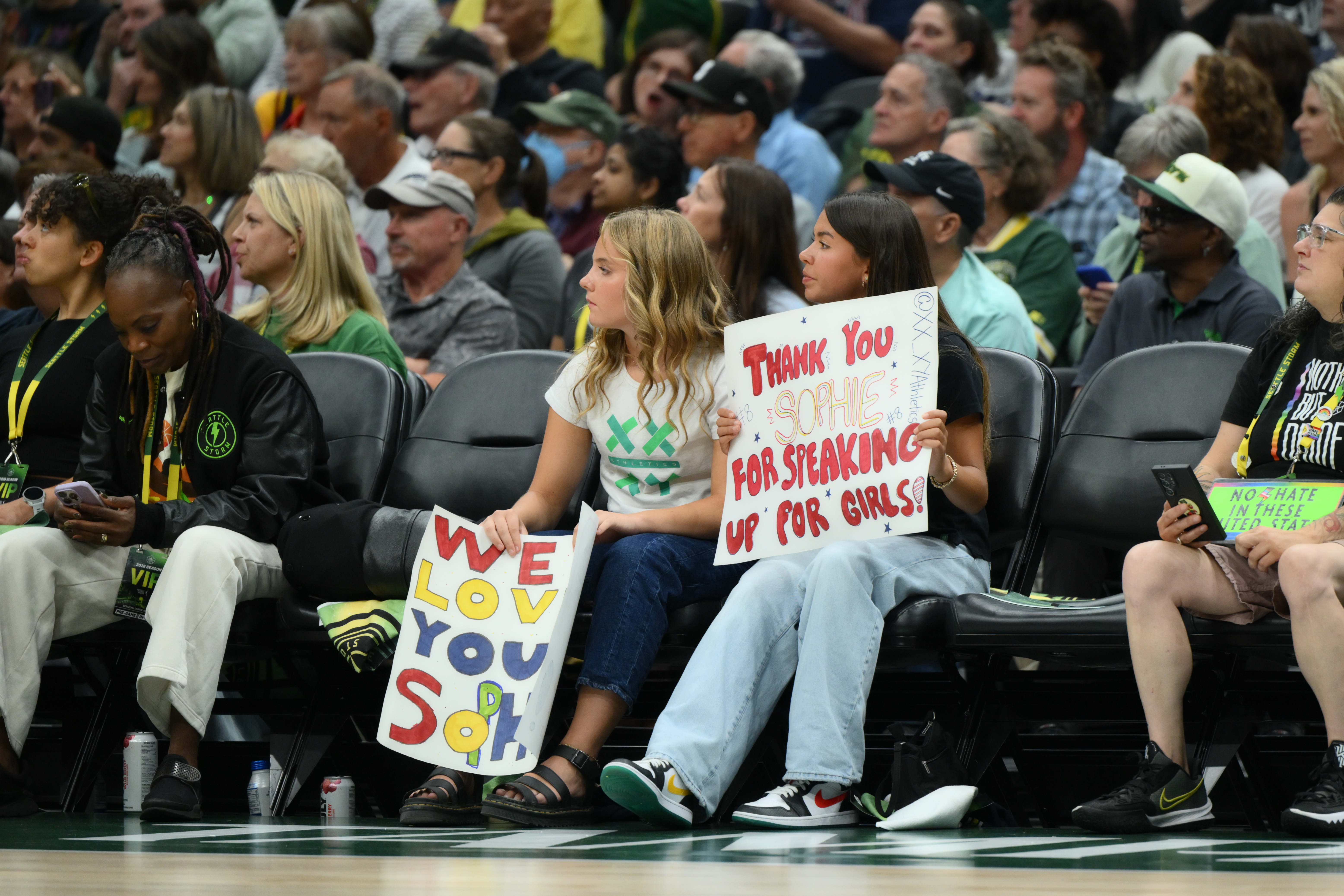 Two girls sit among the fans and hold signs.