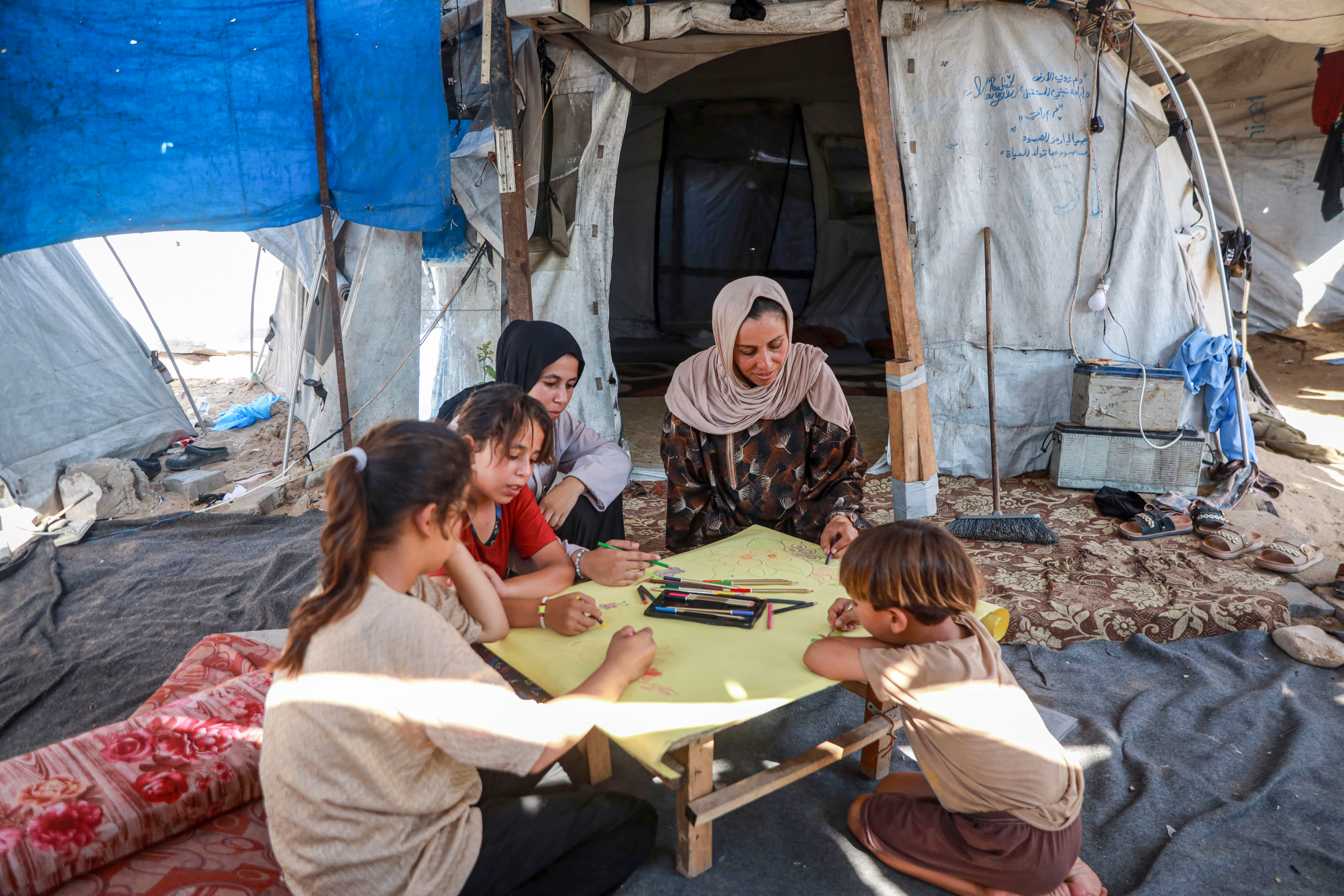 Asmaa Saleh, 41, sits with her children, drawing and coloring together inside their tent in an attempt to create moments of joy during the summer holiday.
