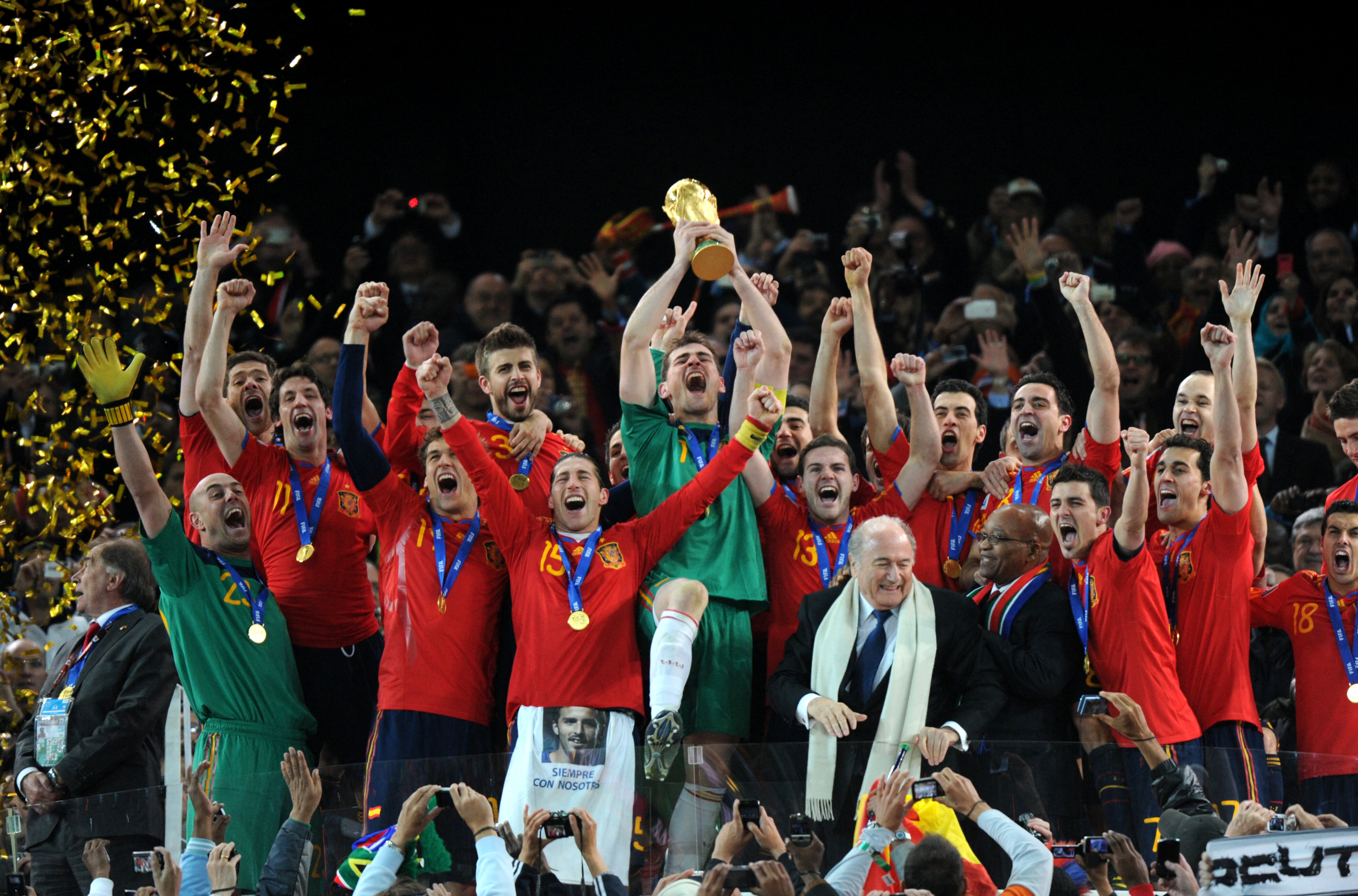 Spain's goalkeeper Iker Casillas (C) raises the trophy as Spain's national football team players celebrate with FIFA President Sepp Blatter (5thR) and South Africas President Jacob Zuma (4thR) winning the 2010 World Cup football final Netherlands vs. Spain on July 11, 2010 at Soccer City stadium in Soweto, suburban Johannesburg. NO PUSH TO MOBILE / MOBILE USE SOLELY WITHIN EDITORIAL ARTICLE - AFP PHOTO / GABRIEL BOUYS (Photo by GABRIEL BOUYS / AFP)