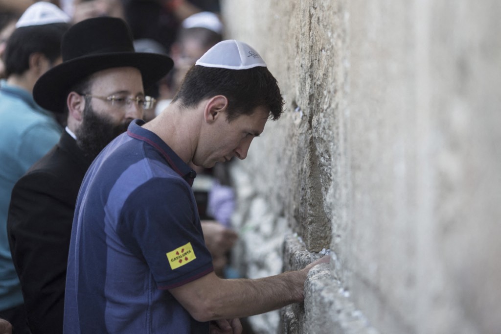 FC Barcelona football player Lionel Messi (R) puts a paper with wishes in a crack in the Western Wall, Judaism's holiest site, in Jerusalem, August 4, 2013. The club is on a two-day visit to Israel and the West Bank. AFP PHOTO/OLIVER WEIKEN-POOL (Photo by OLIVER WEIKEN / POOL / AFP)
