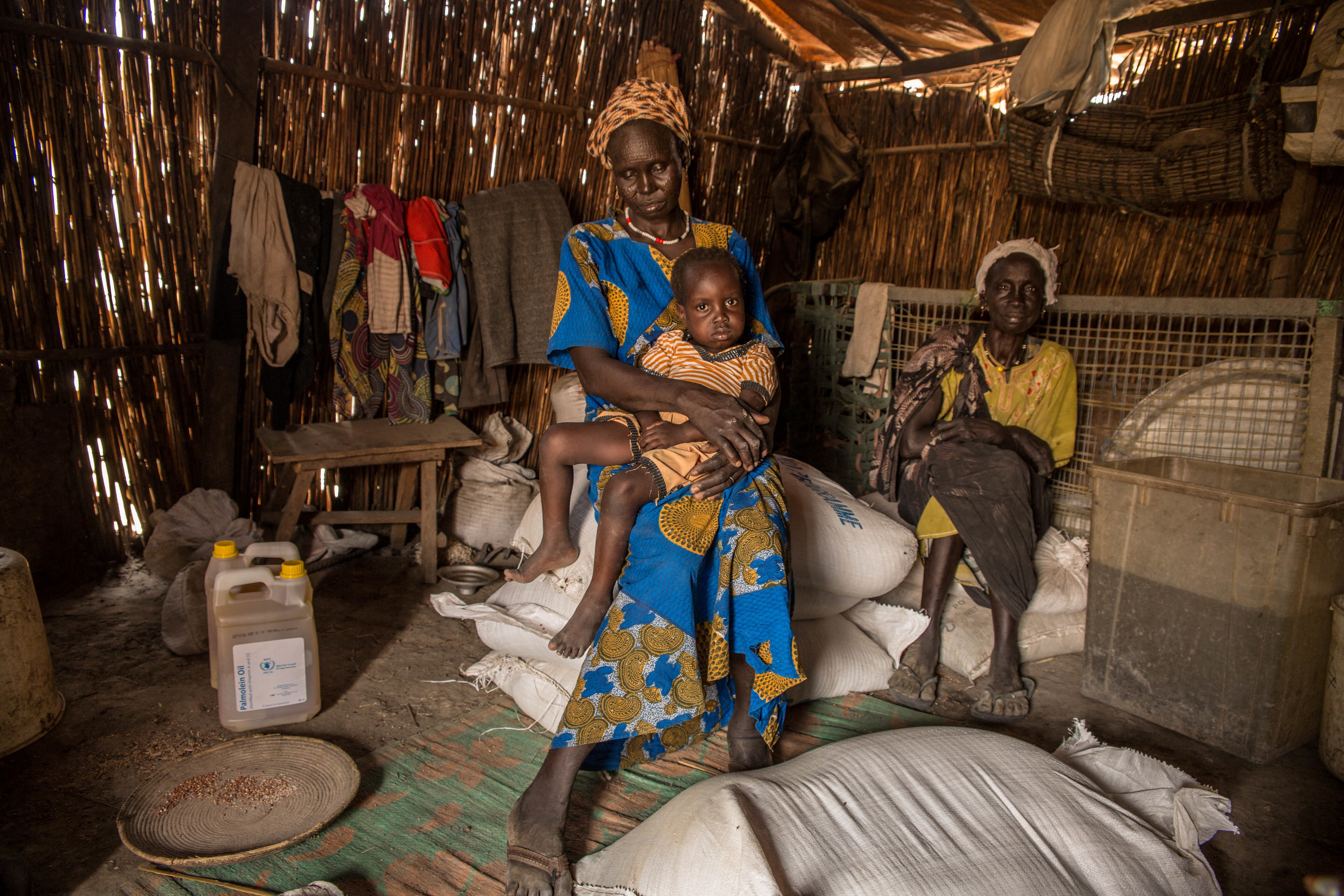 A woman poses with her 3-year-old daughter in their house which is made out of straw, bamboo and plastic sheeting at the Protection of Civilian site (PoC) in Bentiu, South Sudan, on February 15, 2018. Bentiu's Protection of Civilian site was established in January 2014, when 7,000 civilians entered the UNMISS base to seek protection, shortly after the start of the South Sudanese civil war. The camp hosts over 20,000 households and at least 114,250 individuals by IOM. the numbers keep growing every day, as fighting brings more people seeking safety. (Photo by Stefanie GLINSKI / AFP)