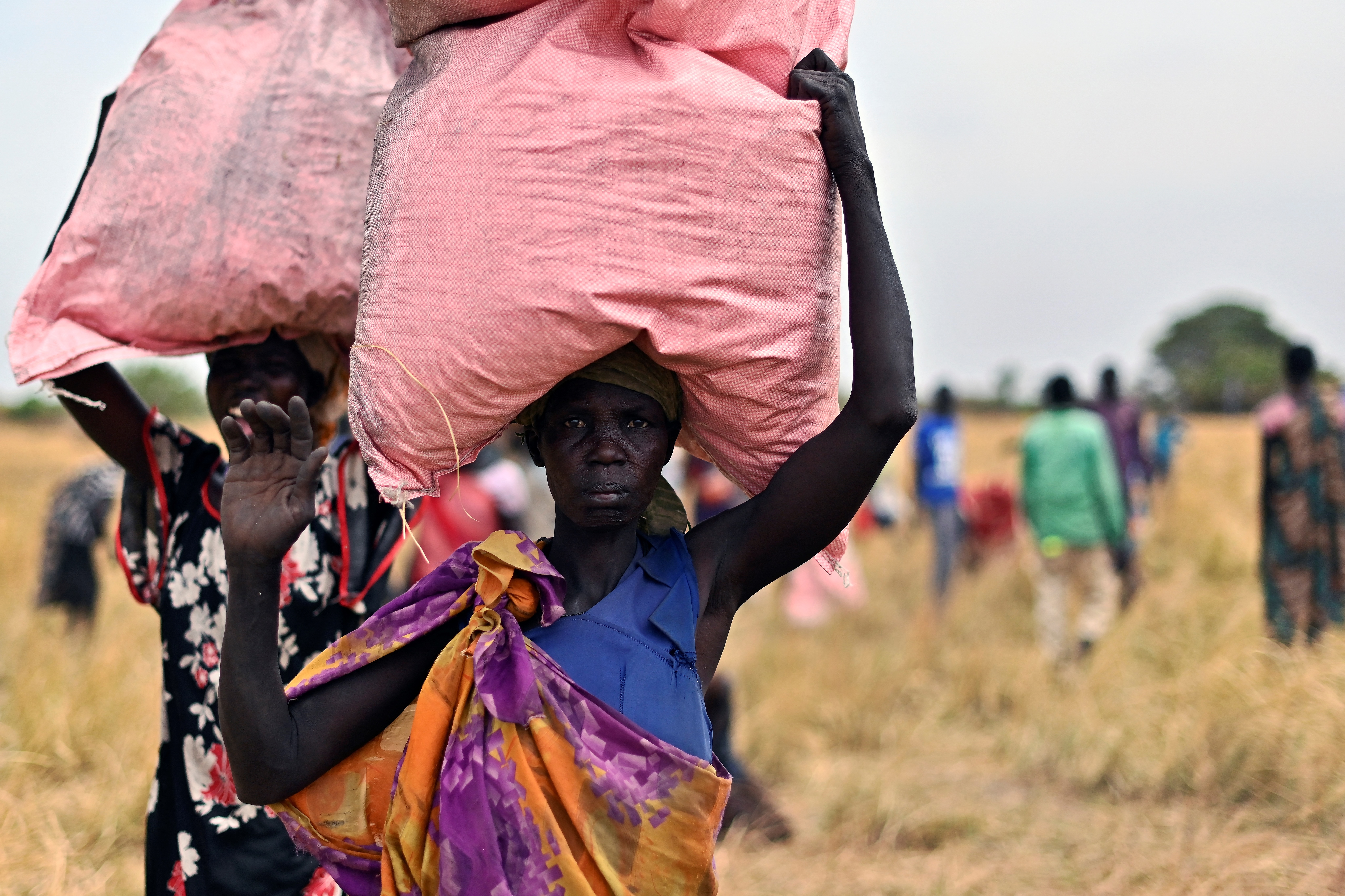 Villagers collect food aid dropped from a plane in gunny bags from a plane onto a drop zone at a village in Ayod county, South Sudan, where World Food Programme (WFP) have just carried out an food drop of grain and supplementary aid on February 6, 2020. The villagers hear the distant roar of jet engines before a cargo plane makes a deafening pass over Mogok, dropping sacks of grain from its hold to the marooned dust bowl below. South Sudan is the last place on earth where food is airdropped, and in Mogok there was little other choice: without the tonnes of grains and cereals, people would have simply perished. (Photo by TONY KARUMBA / AFP)