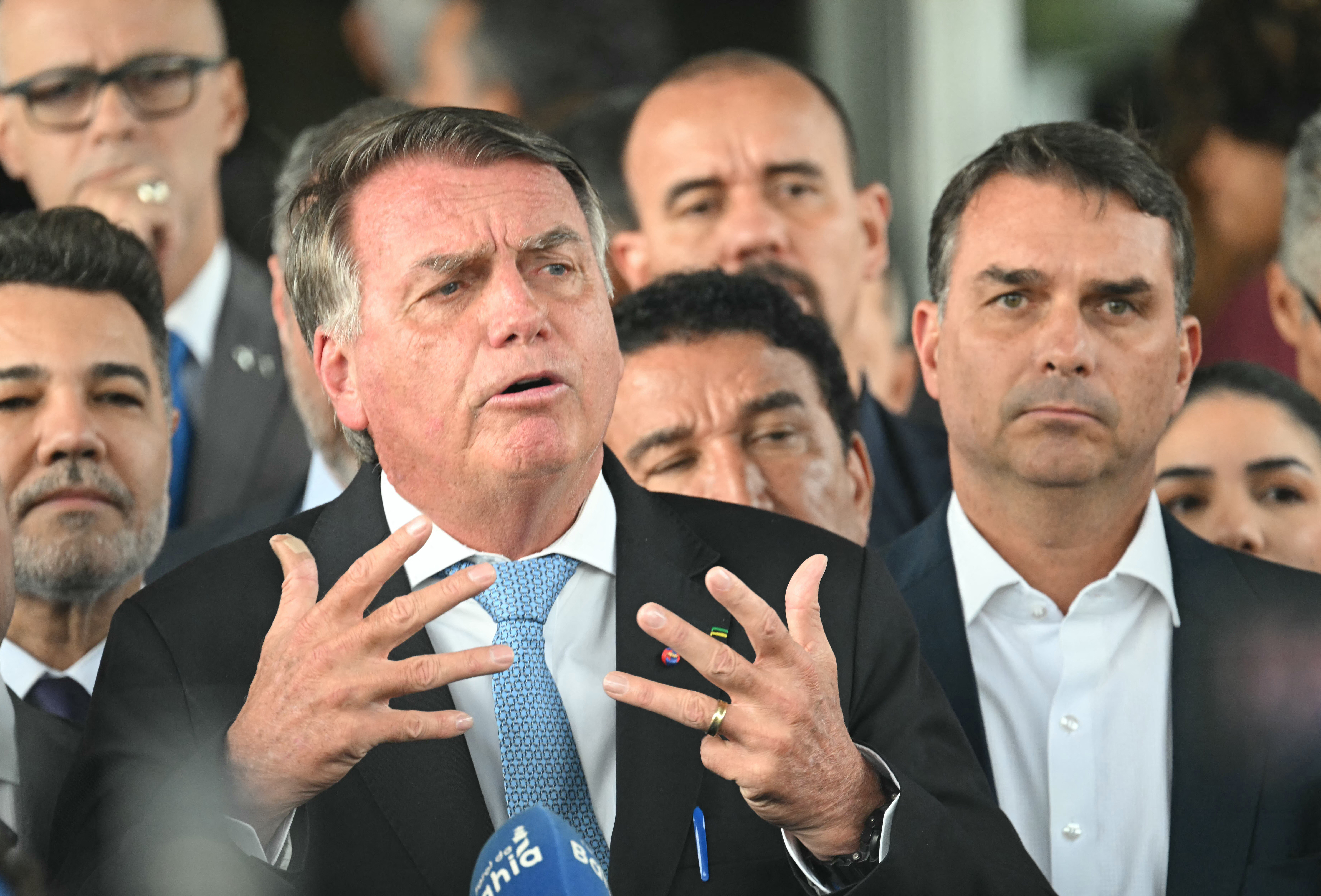 Former Brazil's President Jair Bolsonaro speaks to the media next to his son Senator Flavio Bolsonaro (R), after leaving the Senate building in Brasilia on March 26, 2025. Brazil's Supreme Court on March 26, 2025, ordered far-right ex-president Jair Bolsonaro to stand trial on charges of plotting a coup after failing to win re-election in 2022. (Photo by EVARISTO SA / AFP)