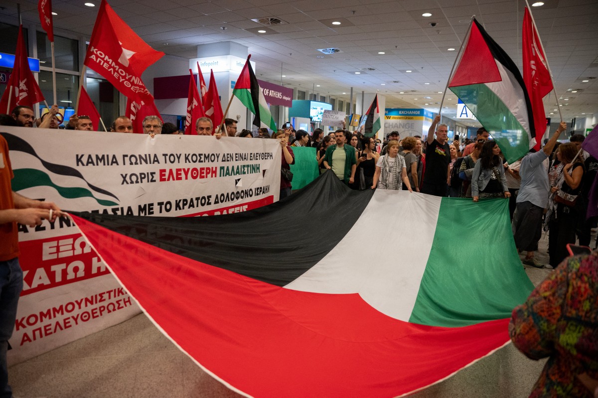 Activists hold a large Palestinian flag as they await the arrival of Greek nationals detained and deported by Israel after the interception of their Gaza-bound flotilla at Athens International airport, in Athens, Greece, on May 22, 2026