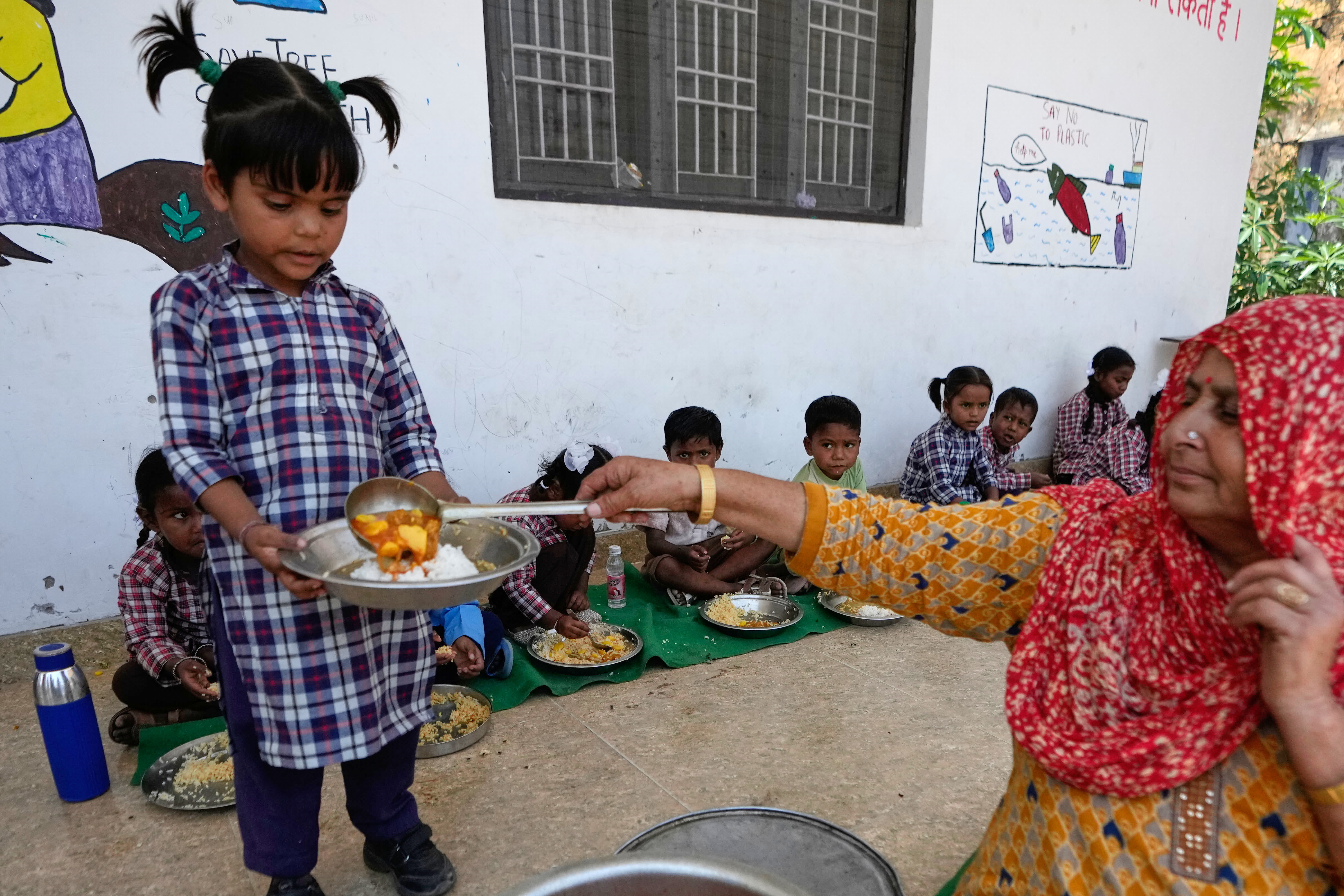 An Indian woman serves vegetable to school children at a government school under the Mid-Day Meal Scheme, in Ganjansoo village near the India Pakistan International Border in Jammu, India, Wednesday, May 13, 2026.(AP Photo/Channi Anand)
