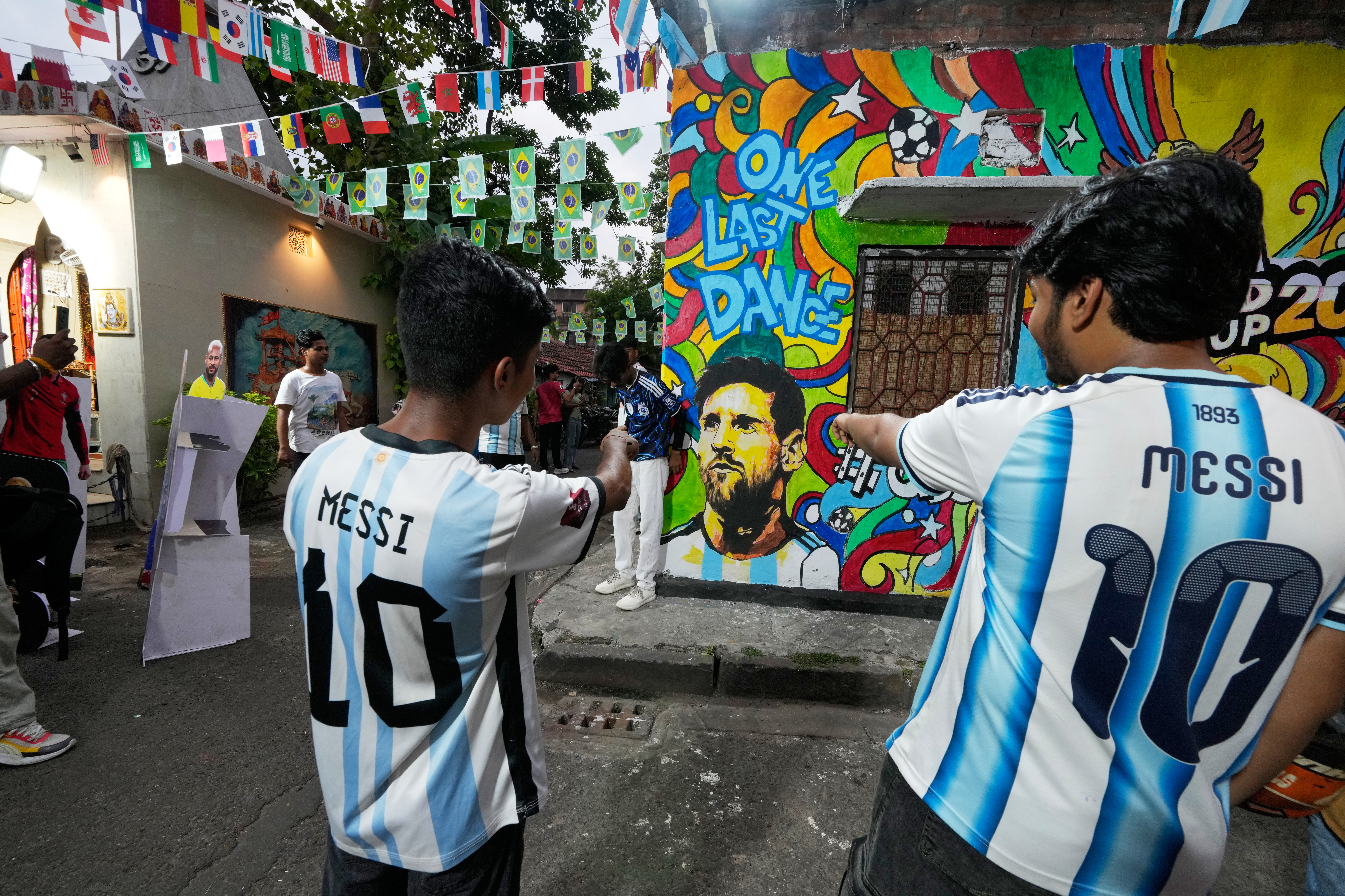 Enthusiasts wearing the No. 10 jersey of Argentina's Lionel Messi point toward wall graffiti celebrating Messi and the World Cup in Kolkata on June 18, 2026 [Bikas Das/AP]