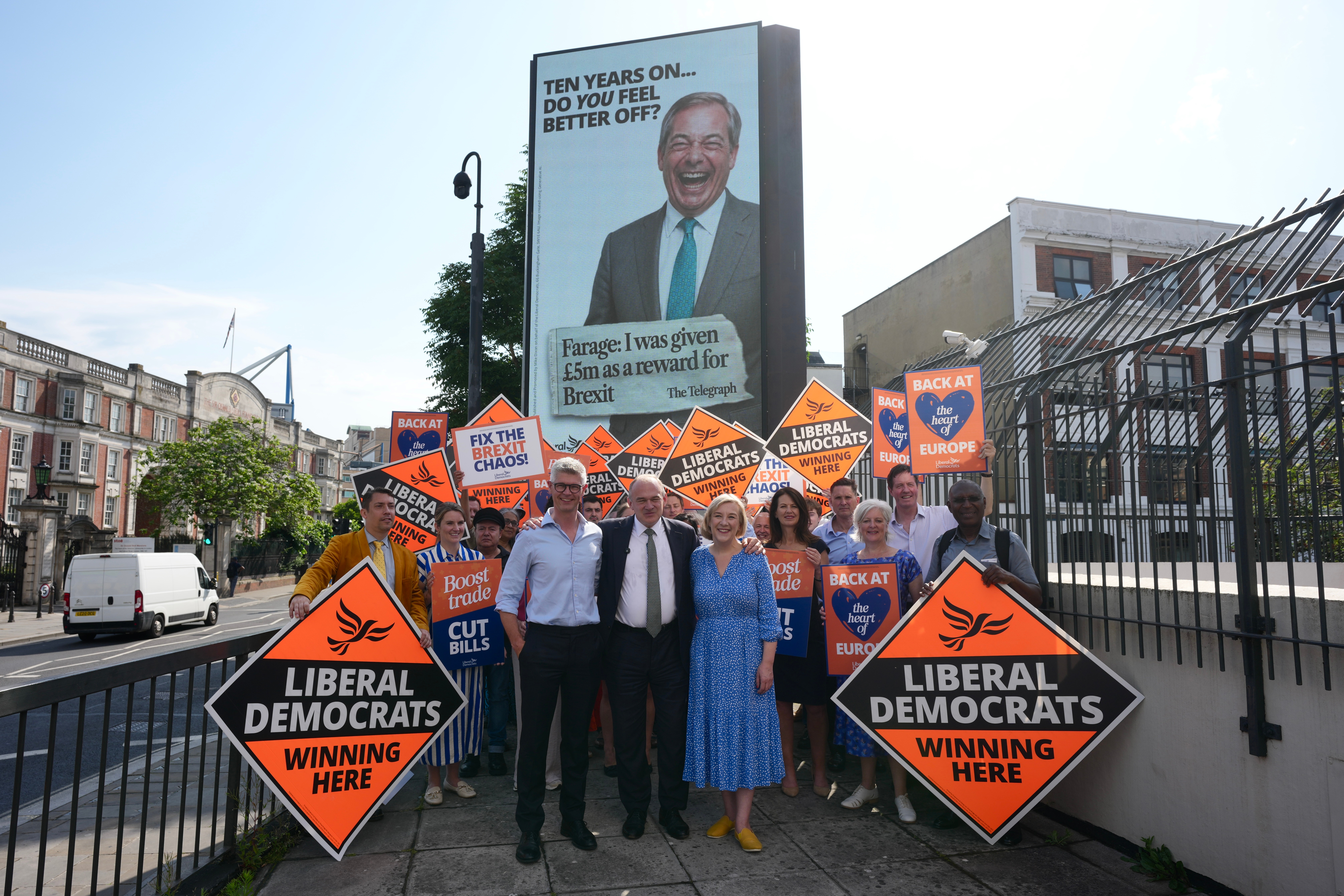 Opposition Liberal Democrats leader Ed Davey, centre, stands in front of a billboard showing Reform UK leader Nigel Farage as he unveils a national campaign to mark the 10th anniversary of the Brexit referendum in London on June 23, 2026