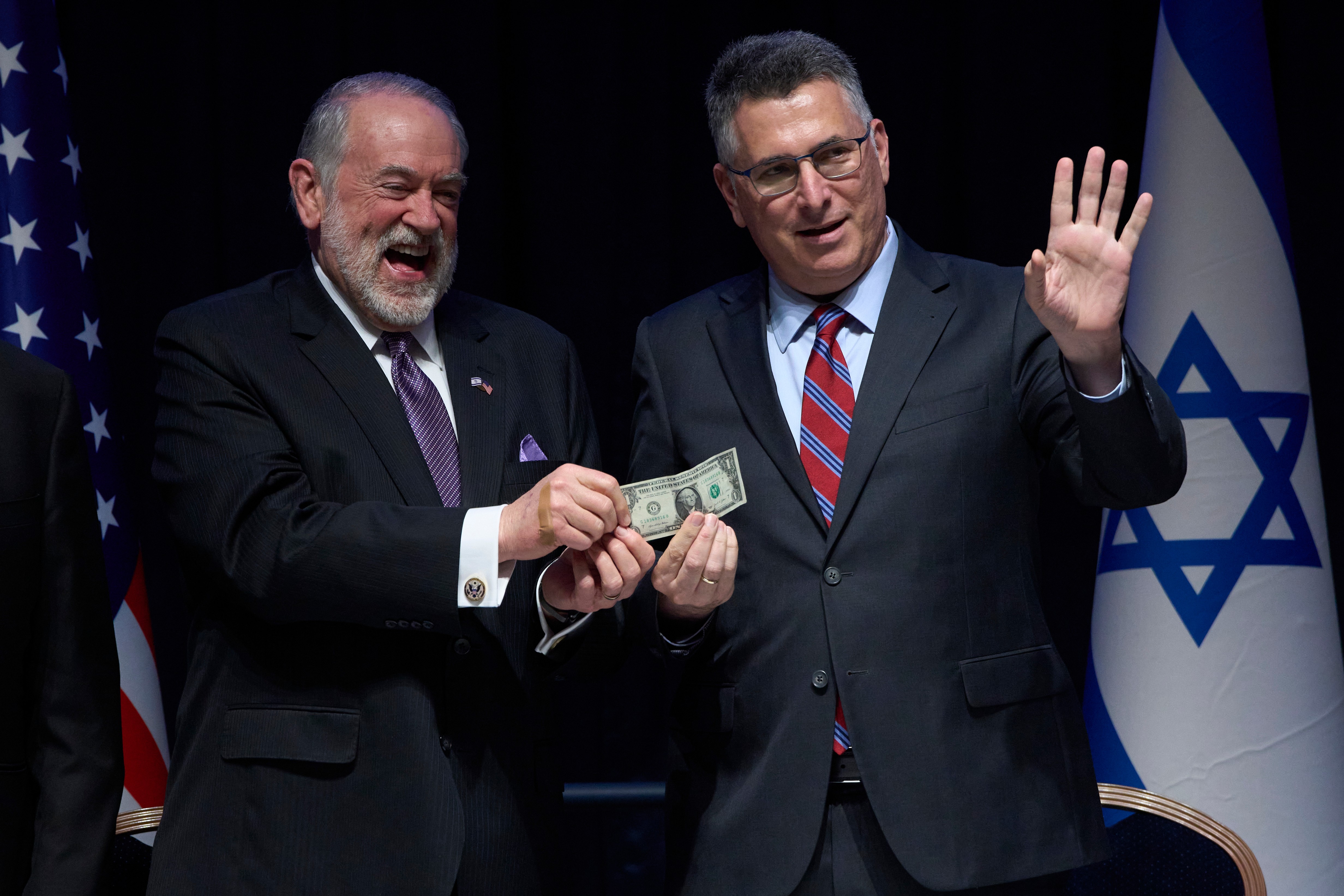 Israeli Foreign Minister Gideon Sa'ar (right) and U.S. Ambassador Mike Huckabee hold up a symbolic one‑dollar bill, the price of leasing the land for the new embassy, during the ceremony in Jerusalem, Wednesday, July 1, 2026. (AP Photo/Ohad Zwigenberg)
