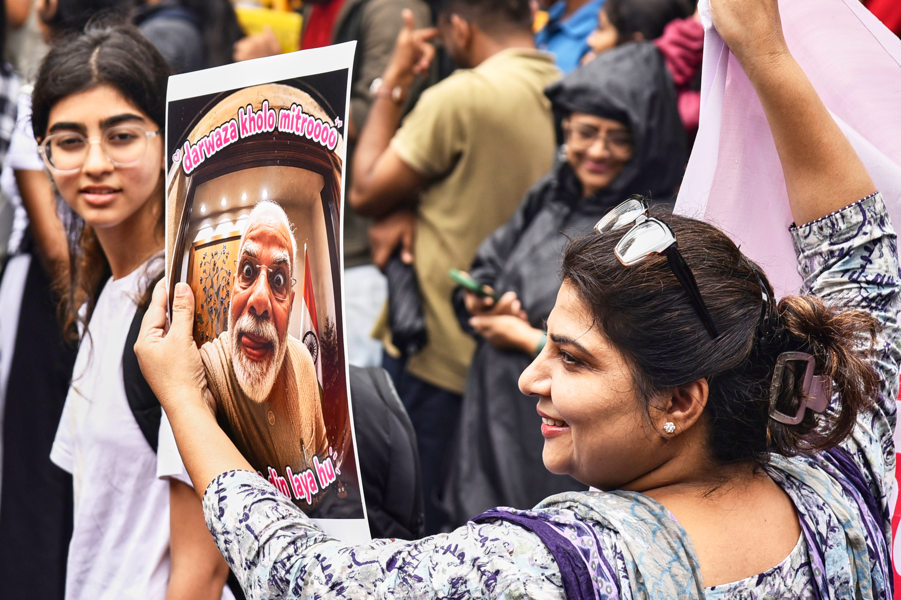 A protester holds a placard with a portrait of Indian Prime Minister Narendra Modi and the text loosely translated as "Open the Door Friends, I Bring Bad Times" during a demonstration demanding educational reforms as part of the Cockroach Janta Party's ongoing protest movement in Pune, India on July 24, 2026.