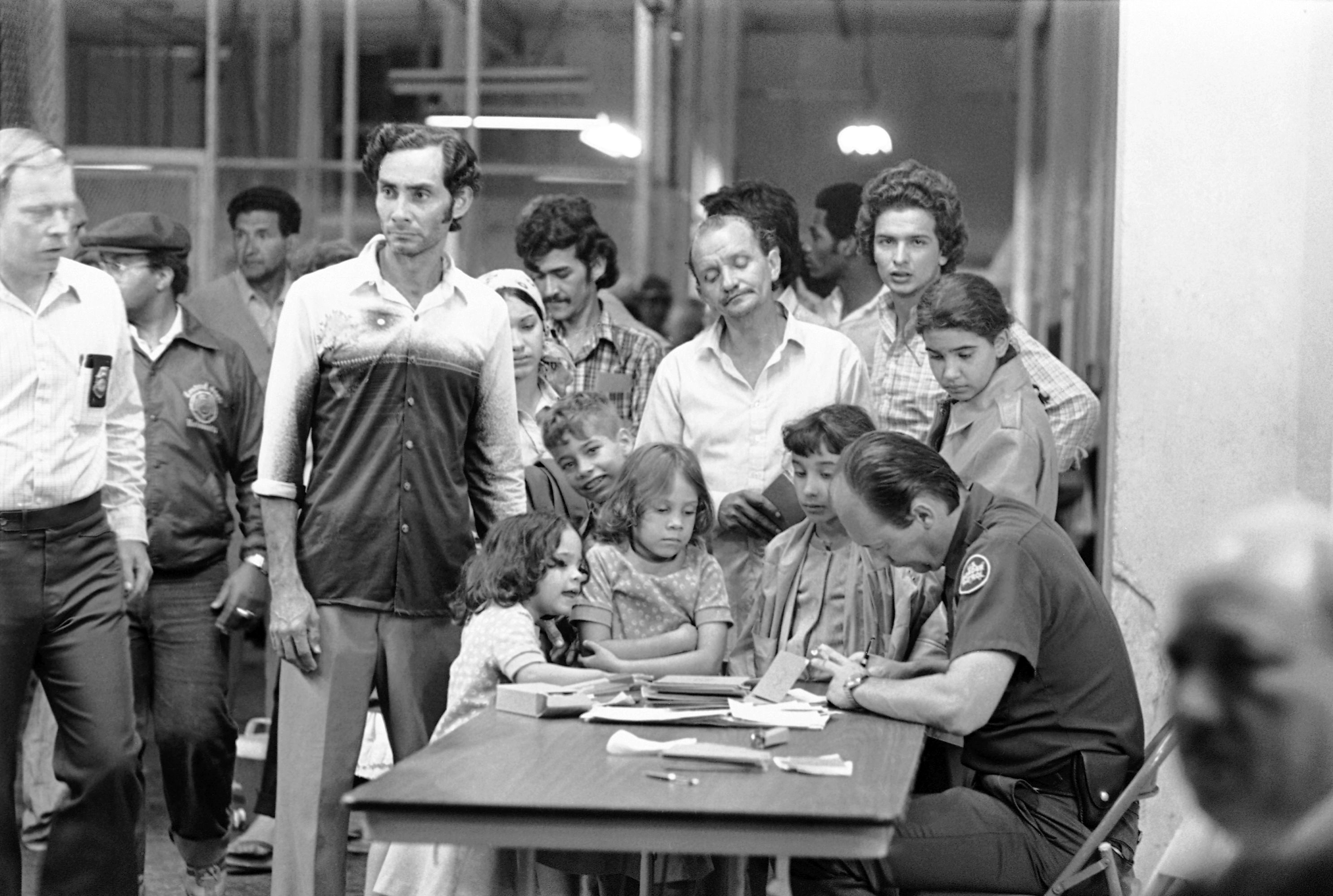 This US Border Patrolman gets a close inspection by young Cuban refugees as they start their processing after arriving at the Key West Naval Base on Wednesday, April 30, 1980 from Mariel, Cuba. Waiting relatives either come to Key West or wait in Miami for their loved ones who escape Communist Cuba aboard packed yachts and trawlers. (AP Photo/PKS)