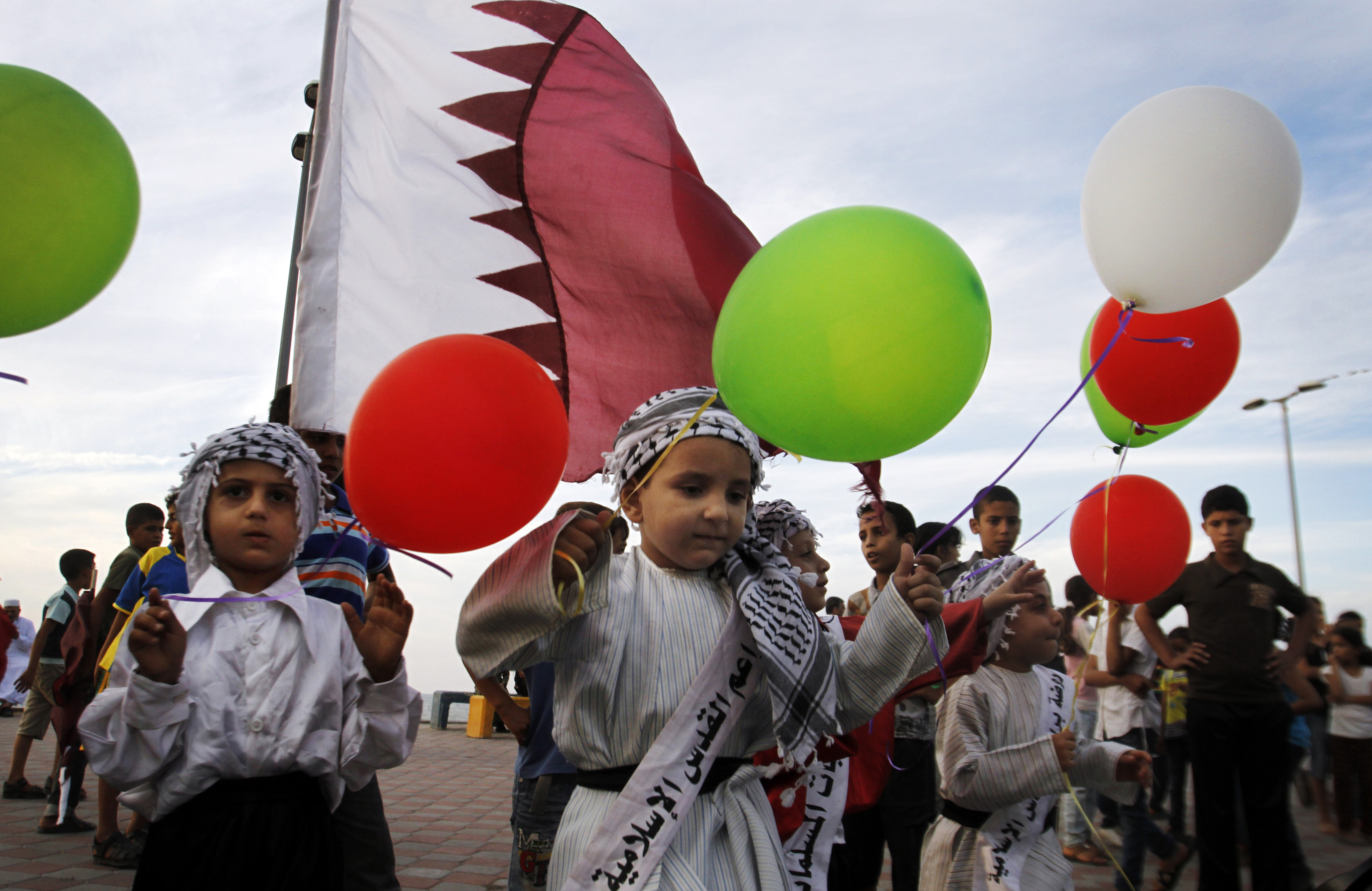Palestinian children wave colored balloons and Qatari flags while waiting for the convoy of Emir of Qatar Sheikh Hamad bin Khalifa al-Thani, not pictured, to pass by a street in Gaza City, Tuesday, Oct. 23, 2012. The emir of Qatar received a hero's welcome in Gaza on Tuesday, becoming the first head of state to visit the Palestinian territory since the Islamist militant Hamas seized control there in 2007. (AP Photo/Hatem Moussa)