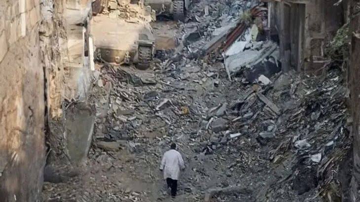 Dr Hussam Abu Safiya wearing a white coat heads towards two Israeli armoured vehicles in a destroyed street in Gaza