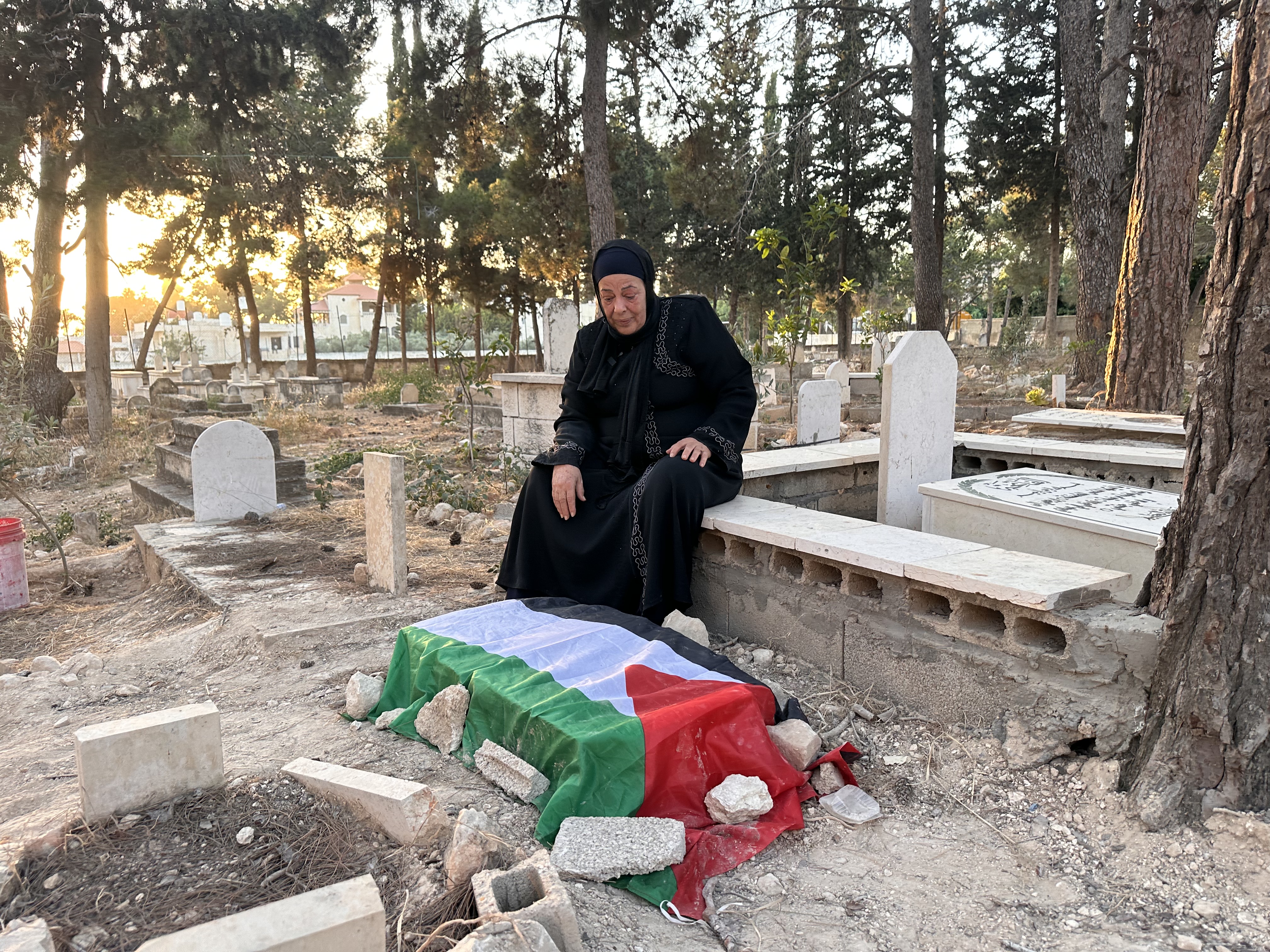 A woman sits beside a grave draped in a Palestinian flag.